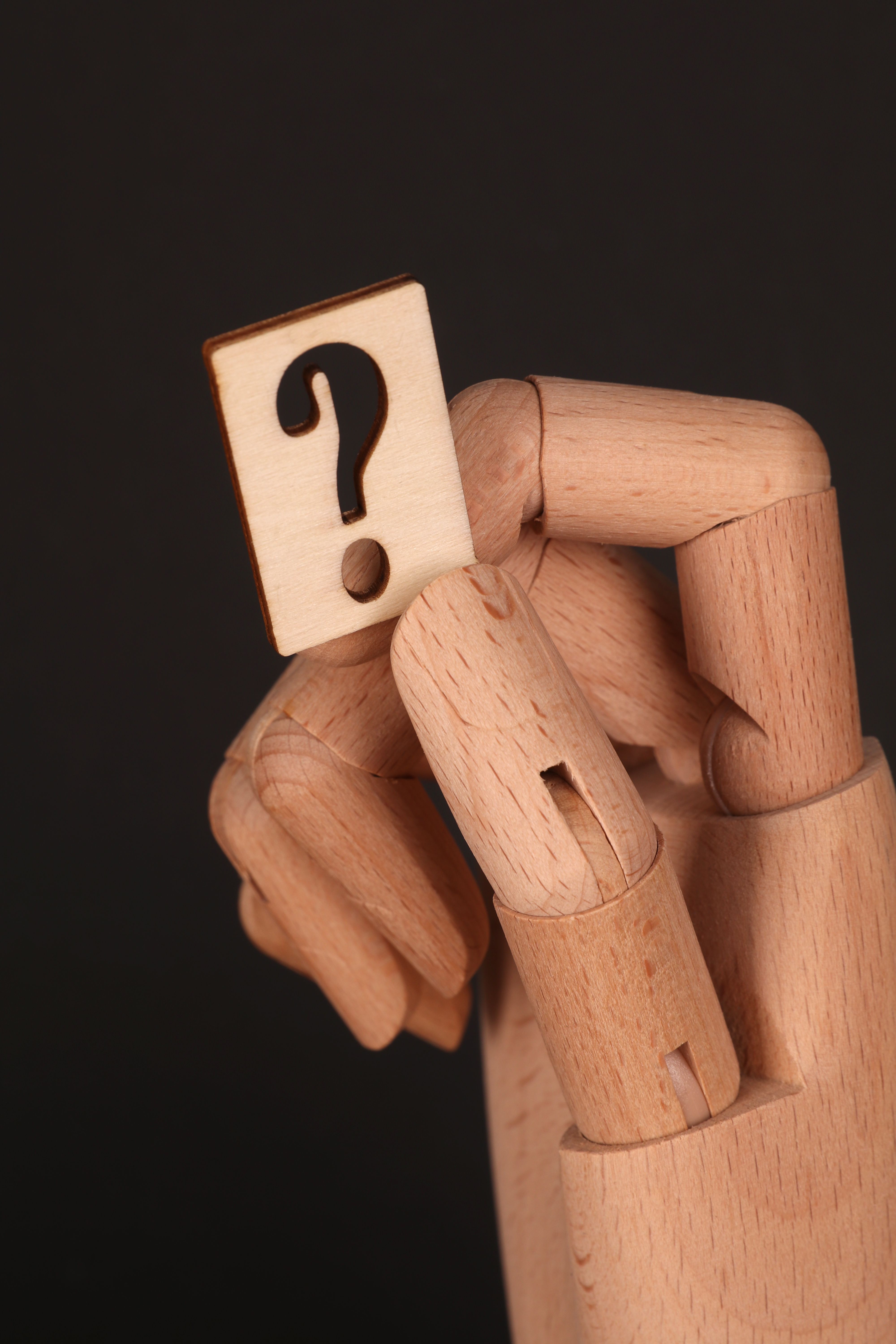 Close-up of a wooden hand holding a question mark on a black background.