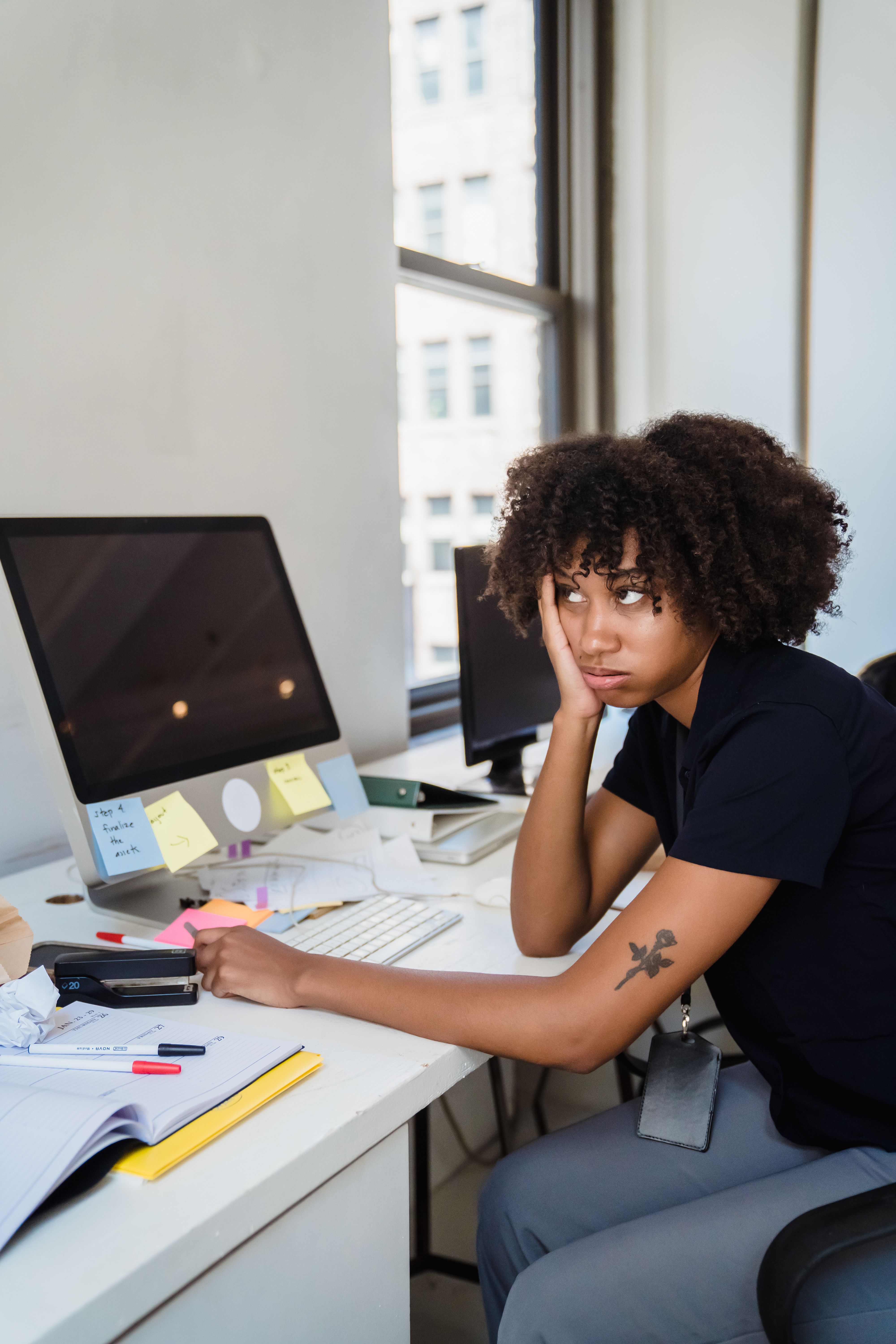 Woman with afro hairstyle looks frustrated at her office desk filled with notes.