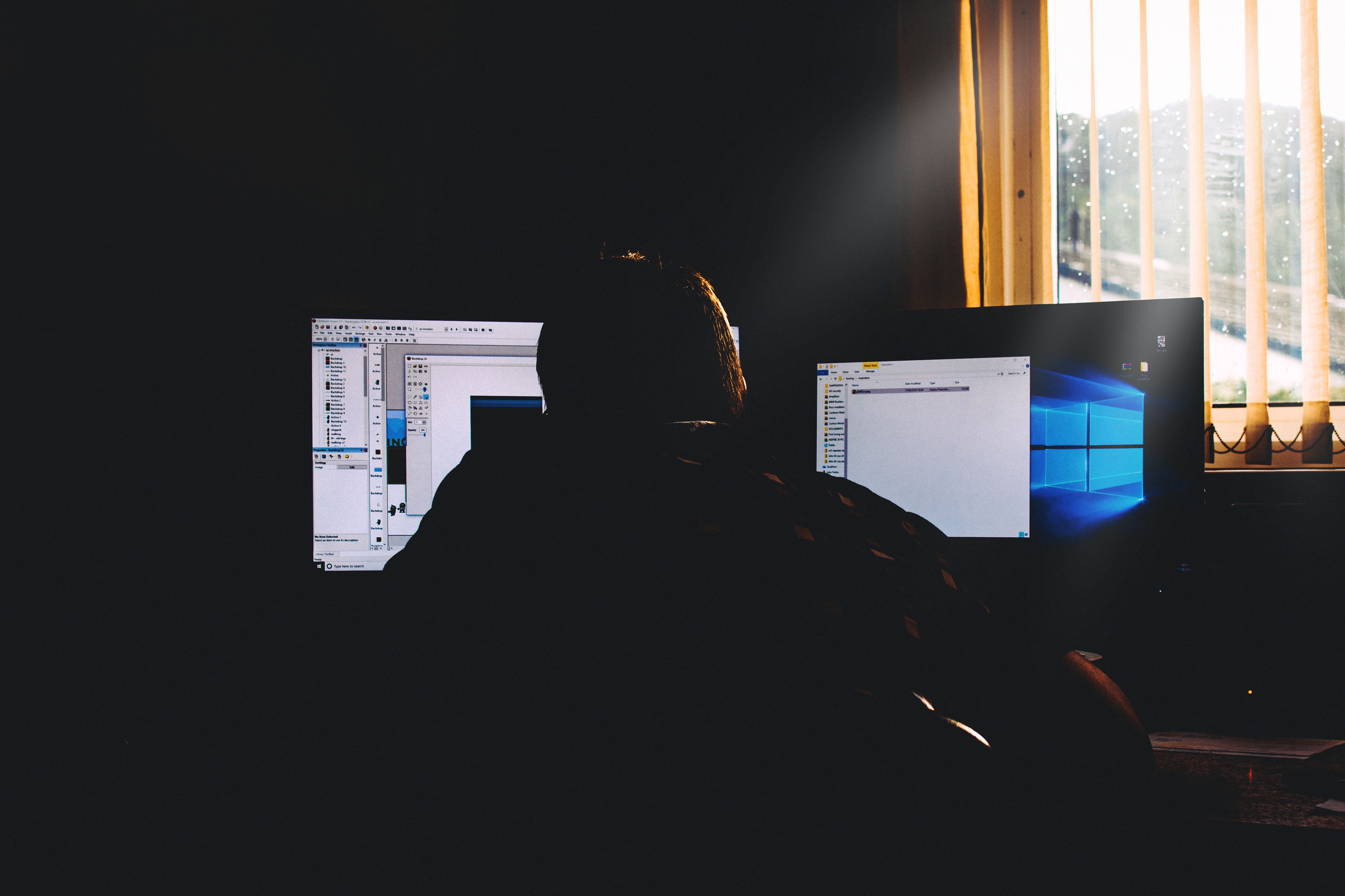 Silhouette of a person working on computers in a dimly lit office environment.