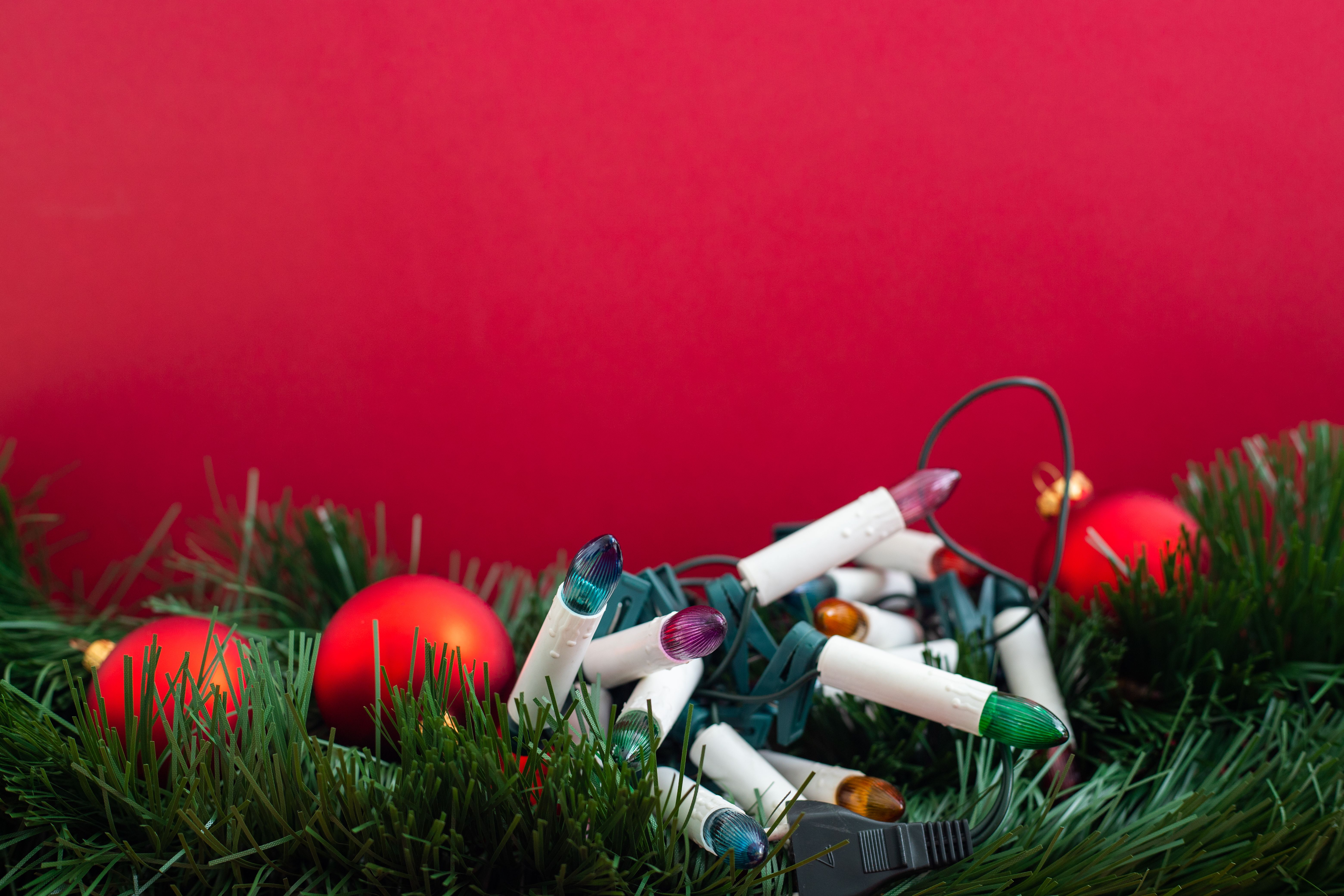 Close-up of Christmas ornaments and colorful lights against a red background.