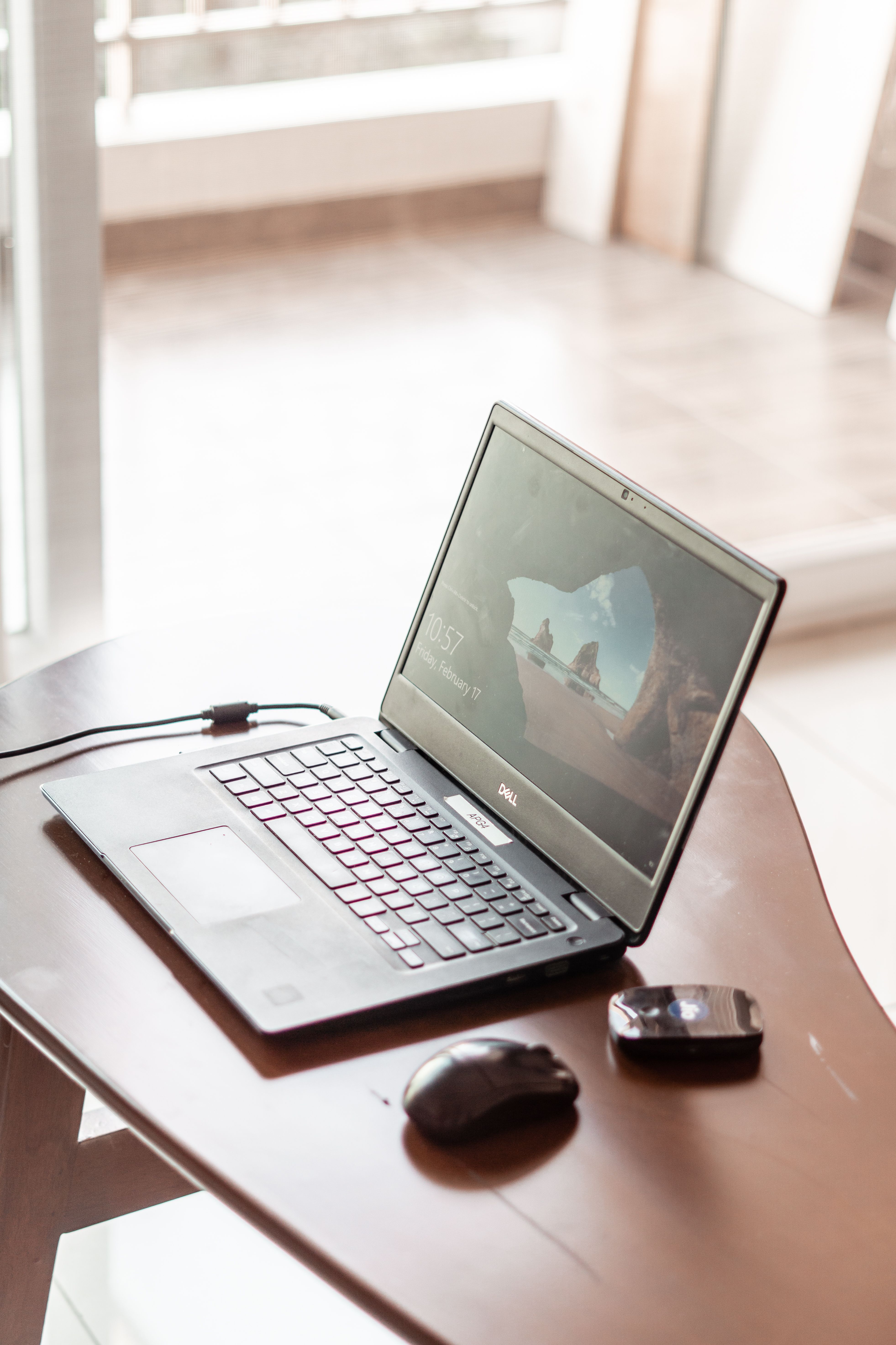 A sleek laptop with mouse on a wooden table in a bright, sunlit room, ideal for work or study.