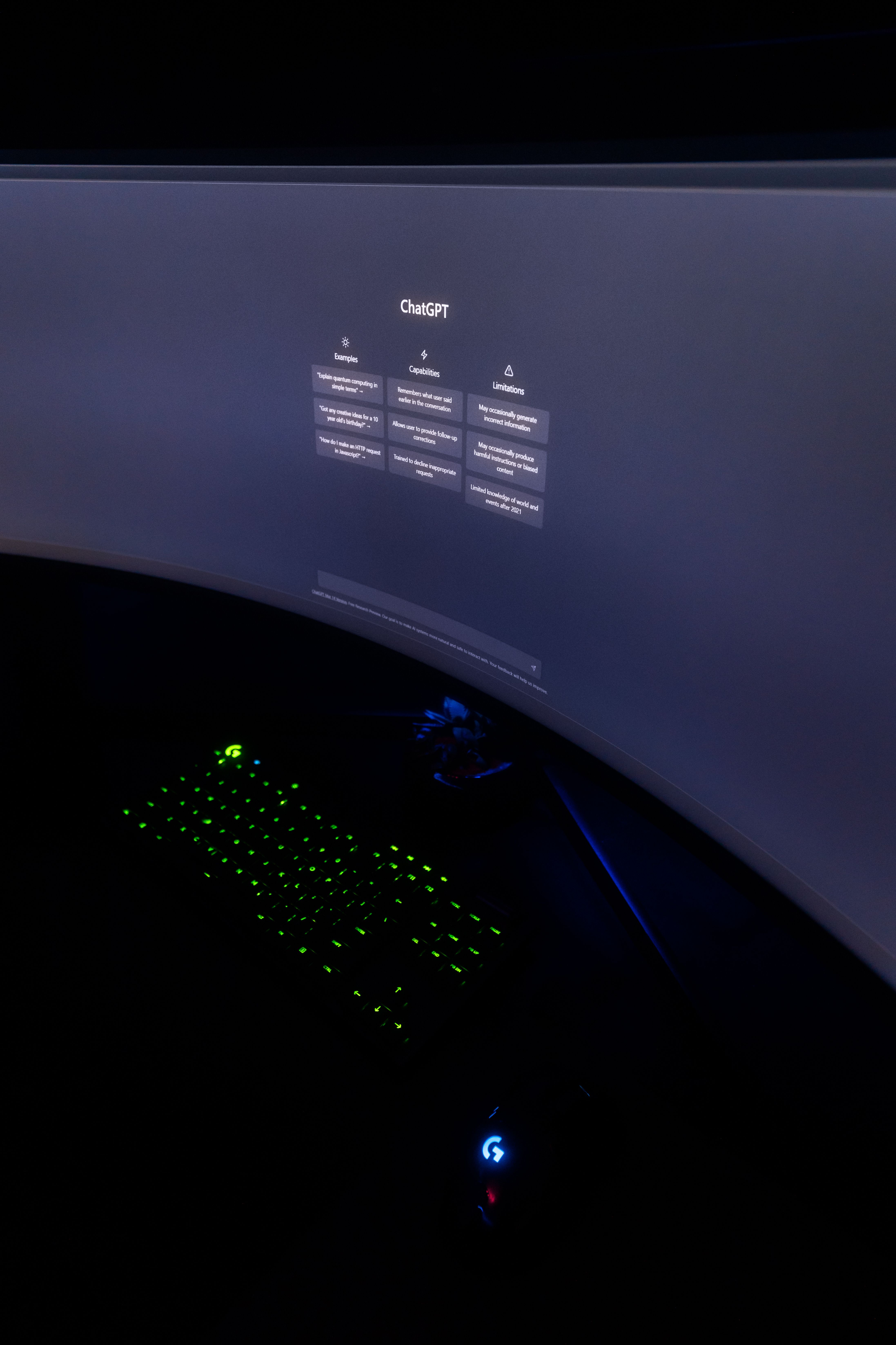 Dimly lit workspace featuring a curved monitor displaying ChatGPT and illuminated keyboard.