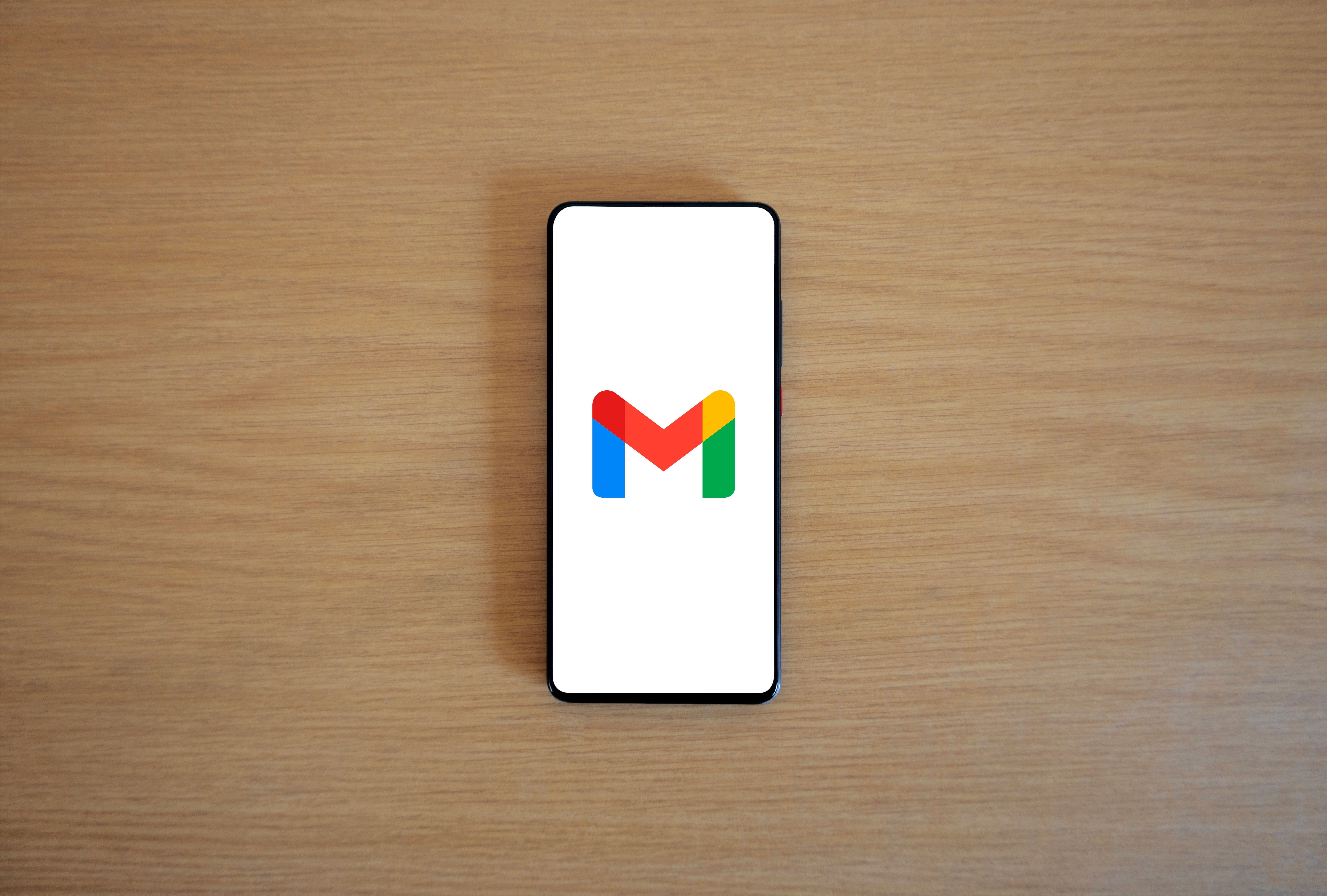 A smartphone displaying the Gmail app logo on a wooden surface, viewed from above.