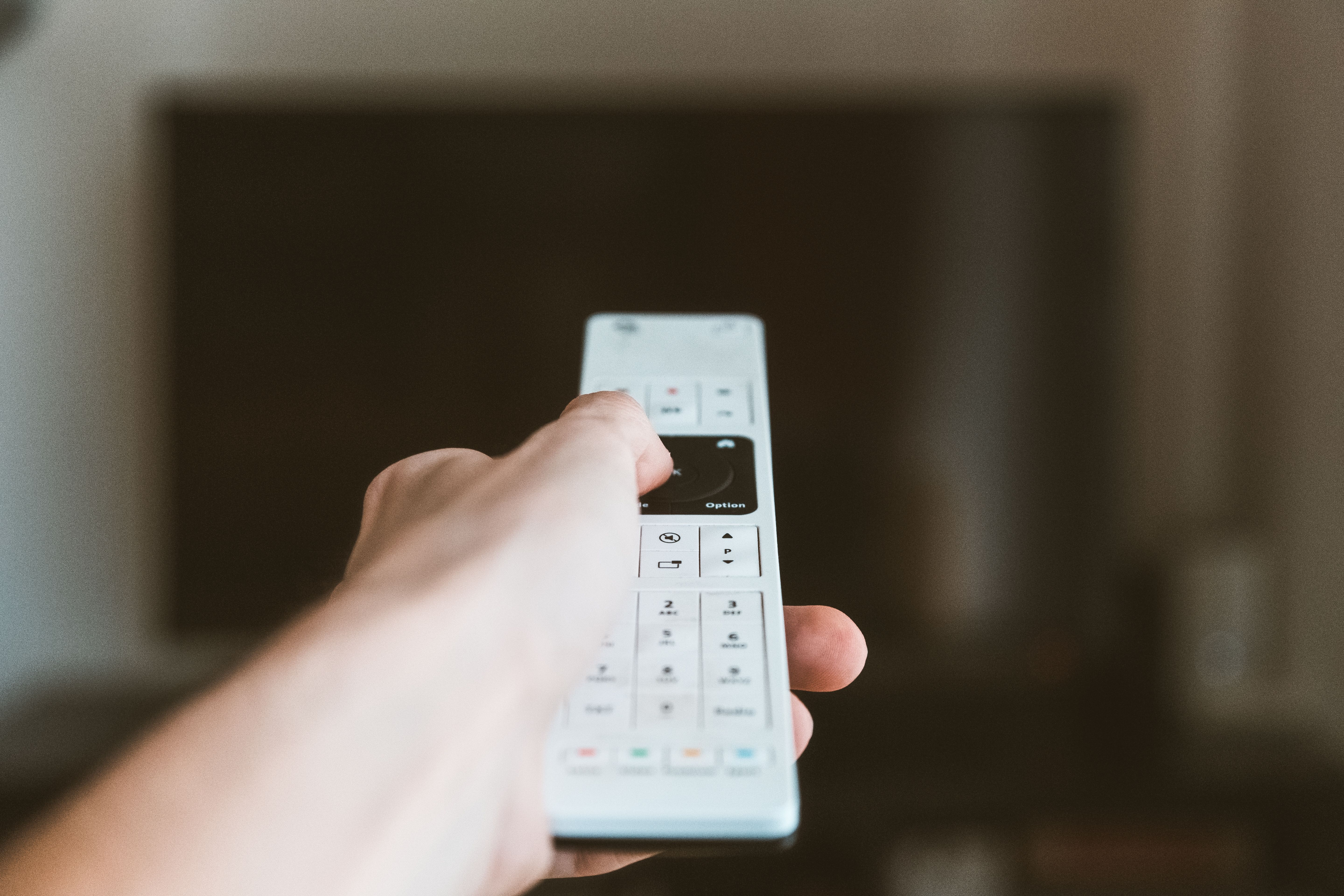 Close-up of a hand using a remote control to operate a television indoors.