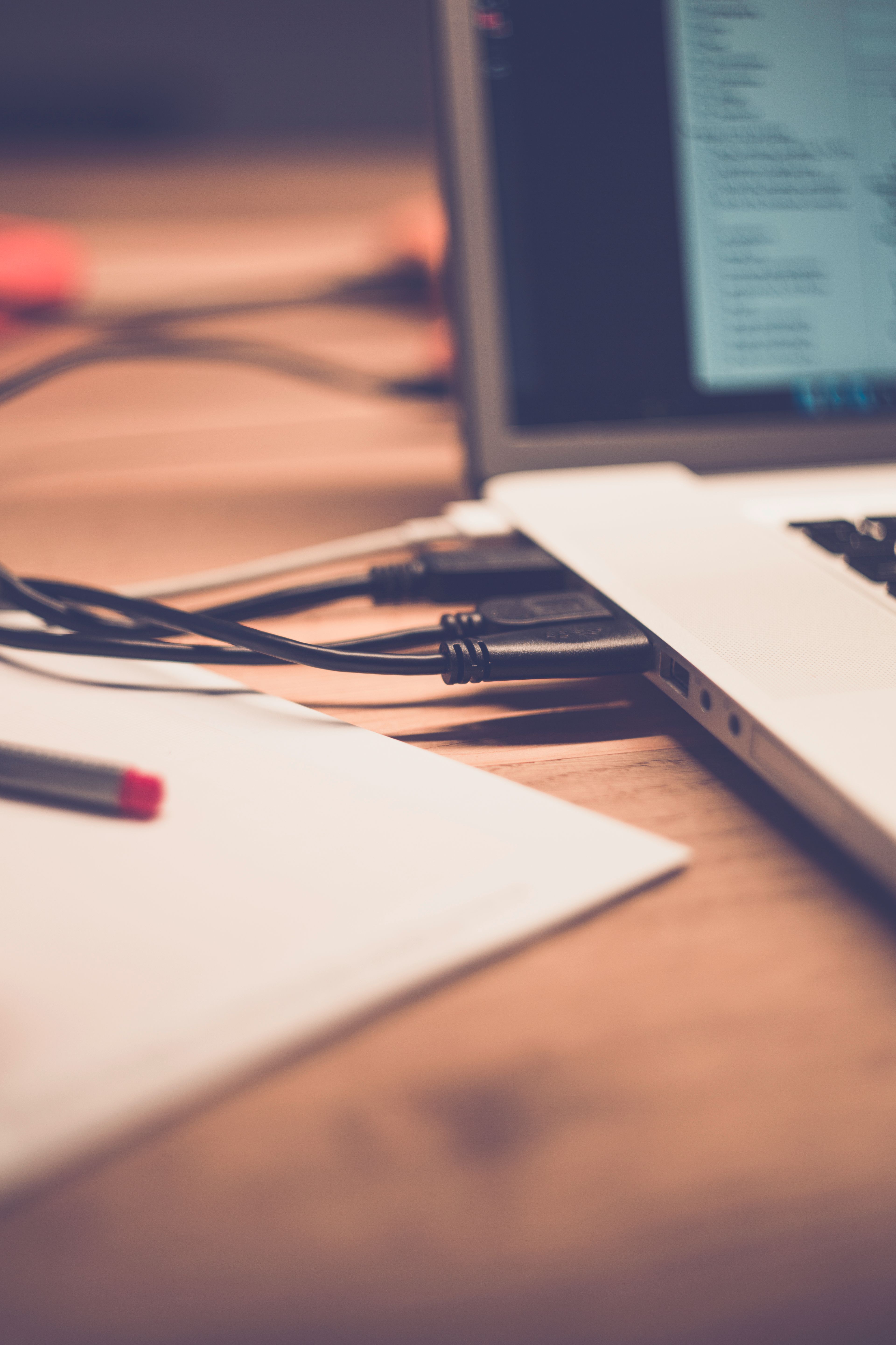 Close-up of laptop with cables on wooden desk, soft focus.