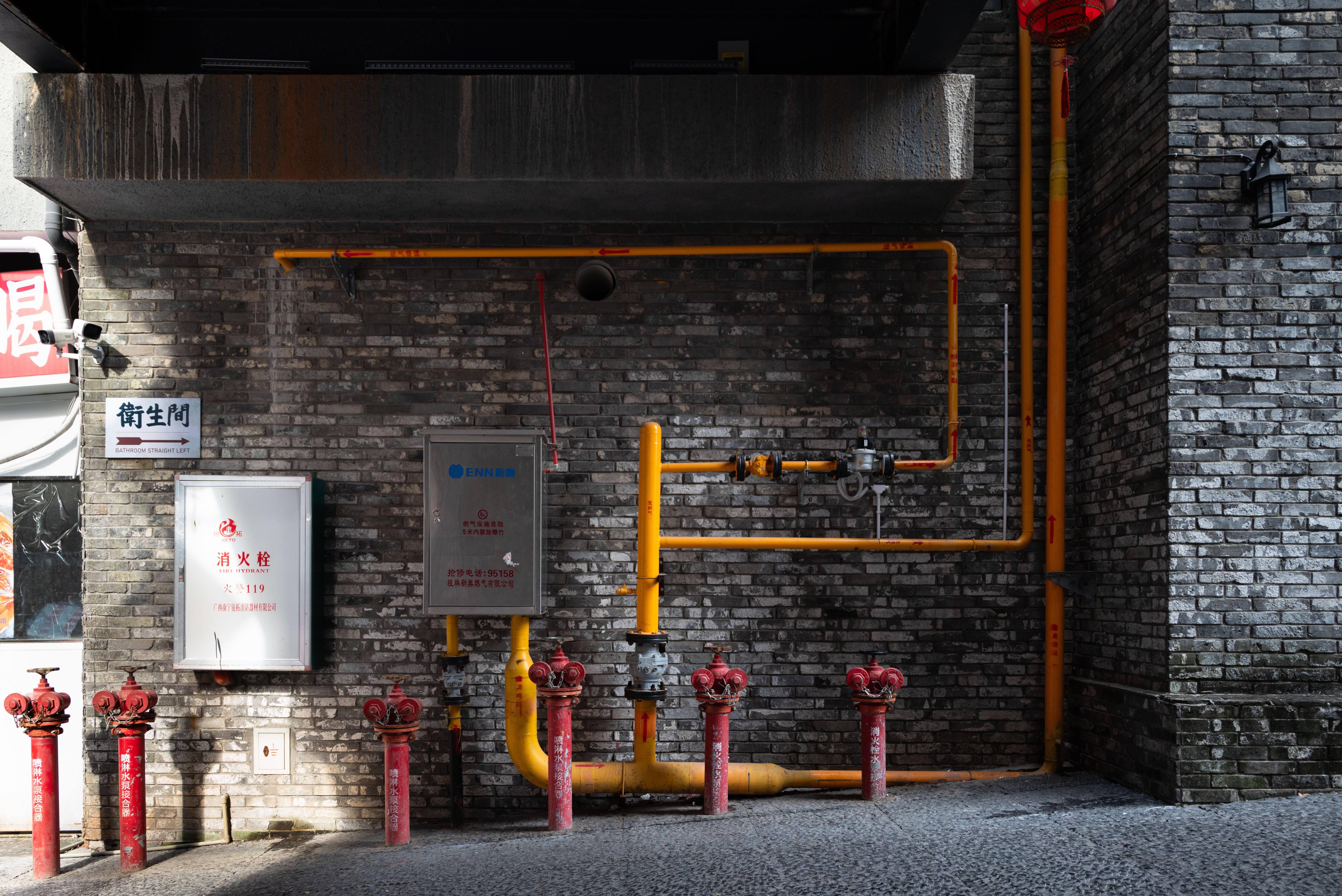Brick wall with red hydrants and yellow piping in an urban alleyway setting.