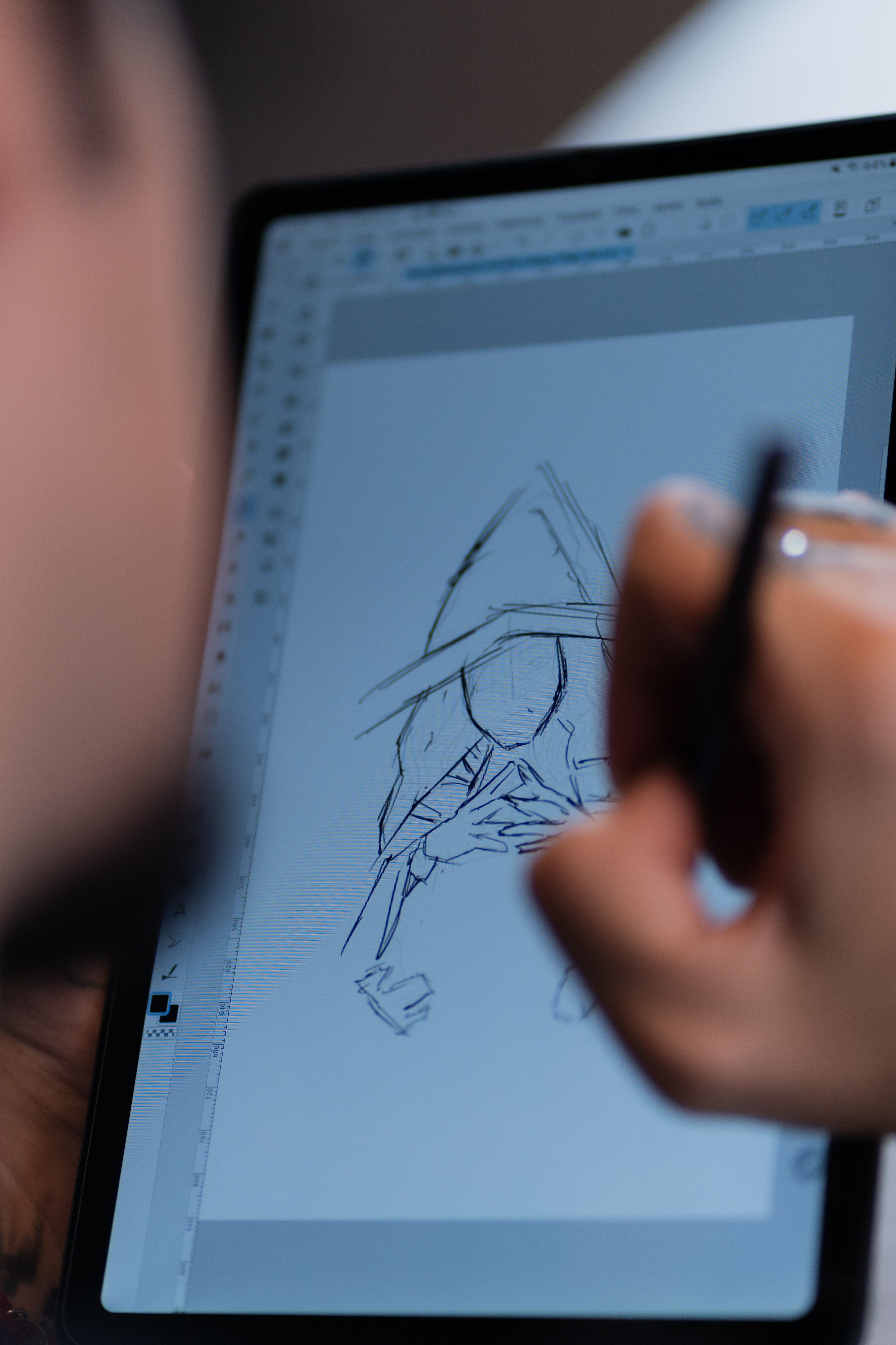 Close-up of digital artist sketching a hooded figure on a tablet, showcasing creative process.