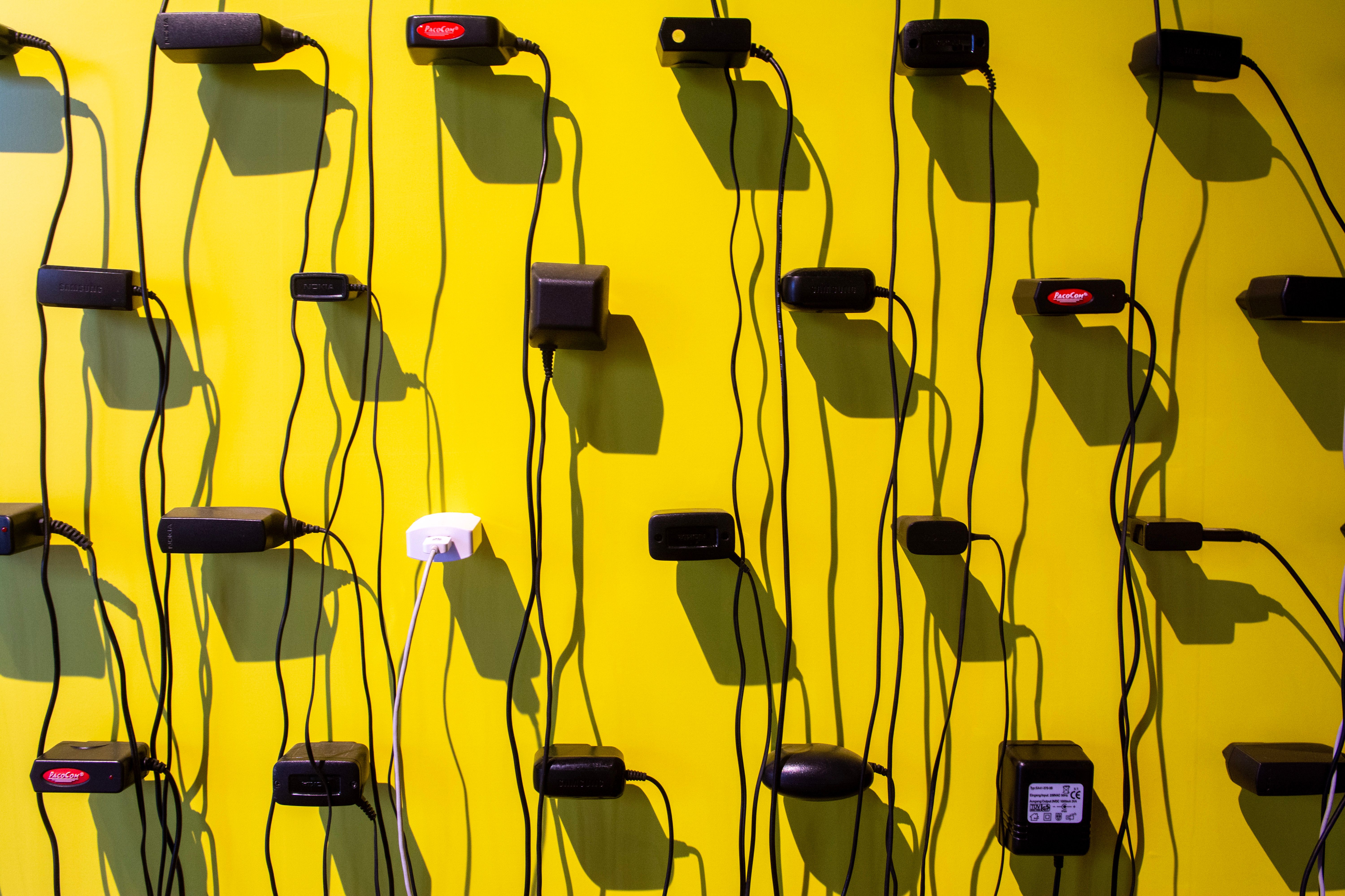 Power adapters casting shadows on a vibrant yellow wall, creating a geometric pattern.