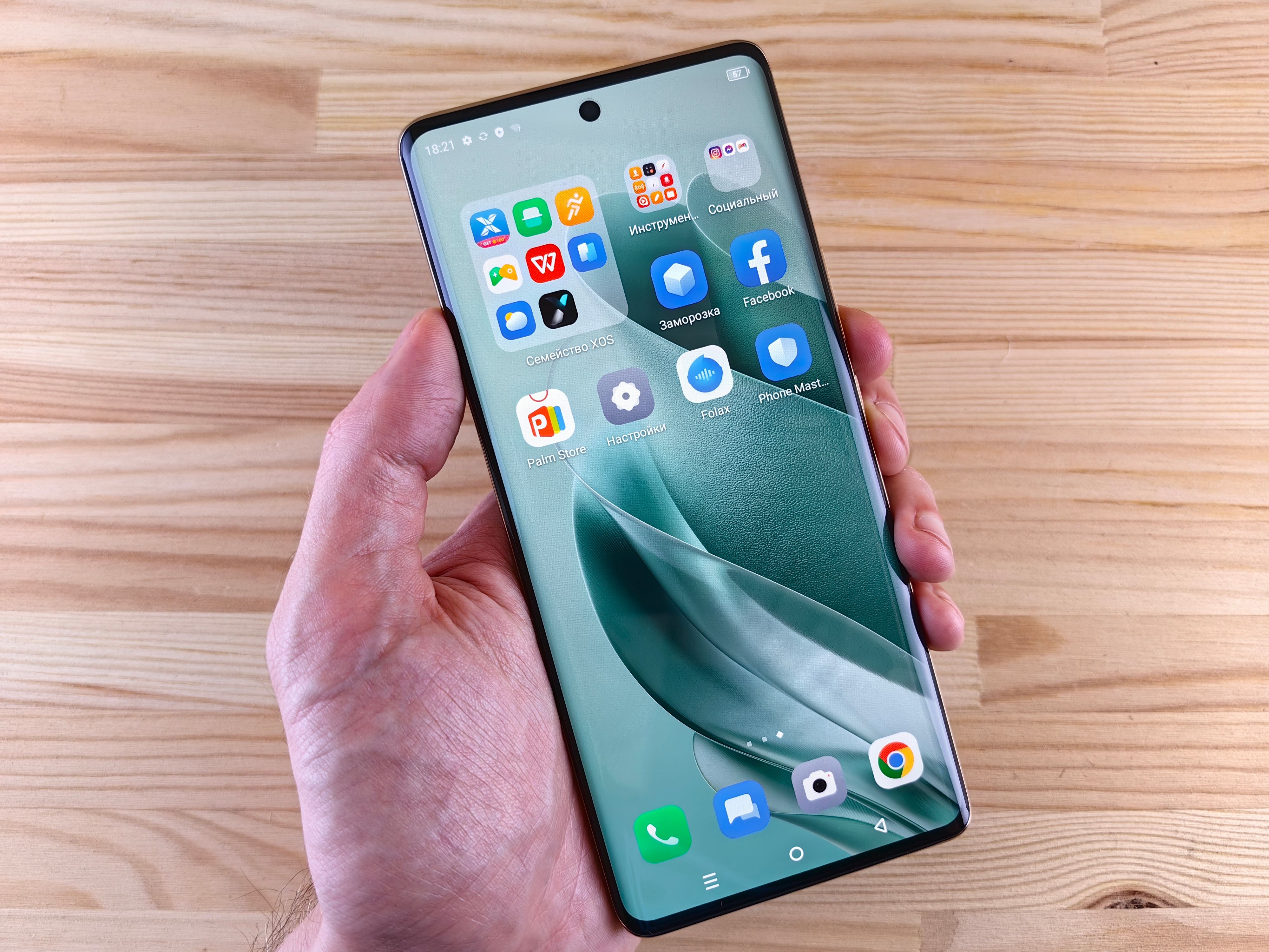 A person holds a modern smartphone with apps displayed on screen, set against a wooden background.