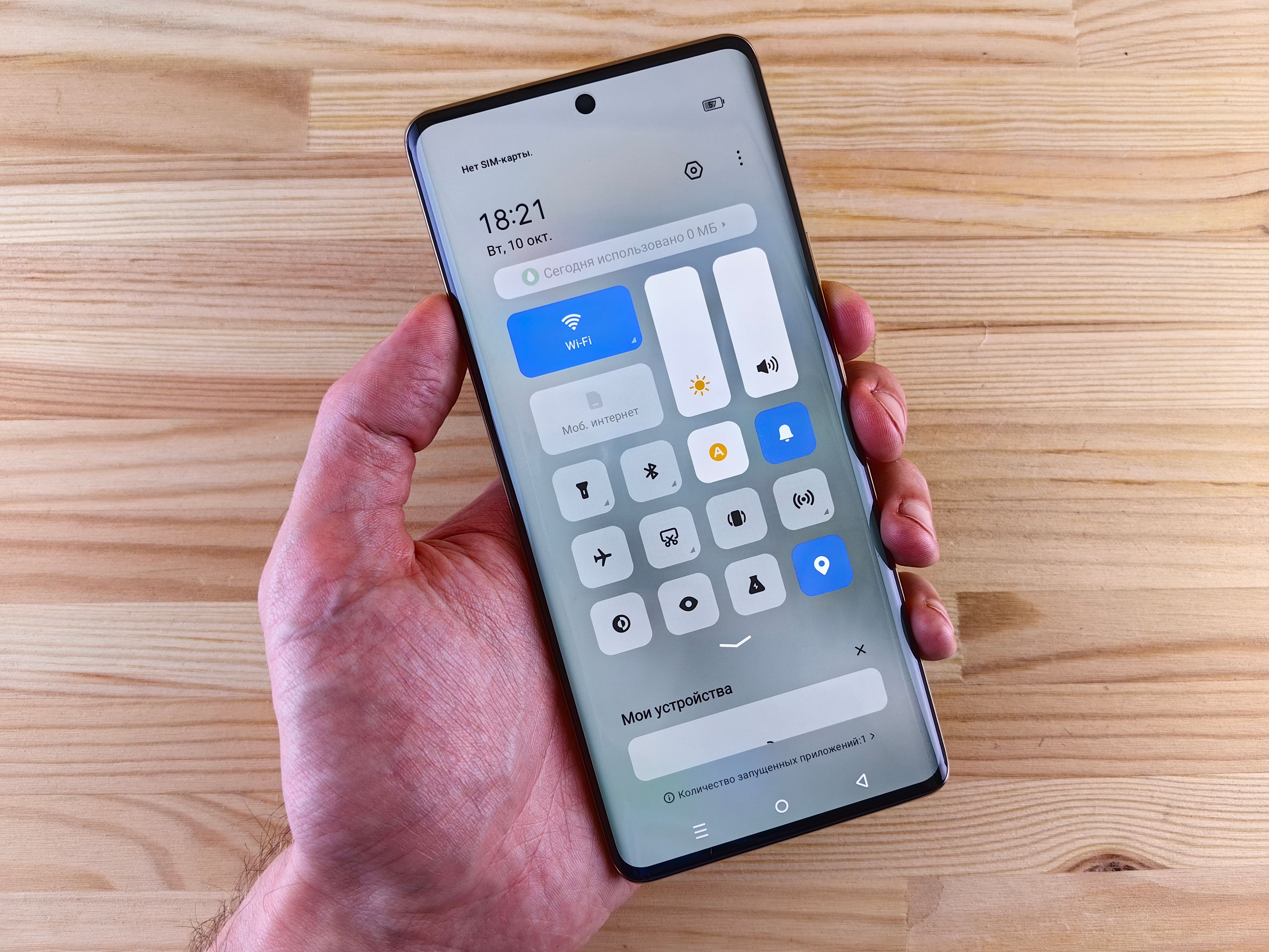 A hand holding a smartphone displaying the control center against a wooden backdrop.