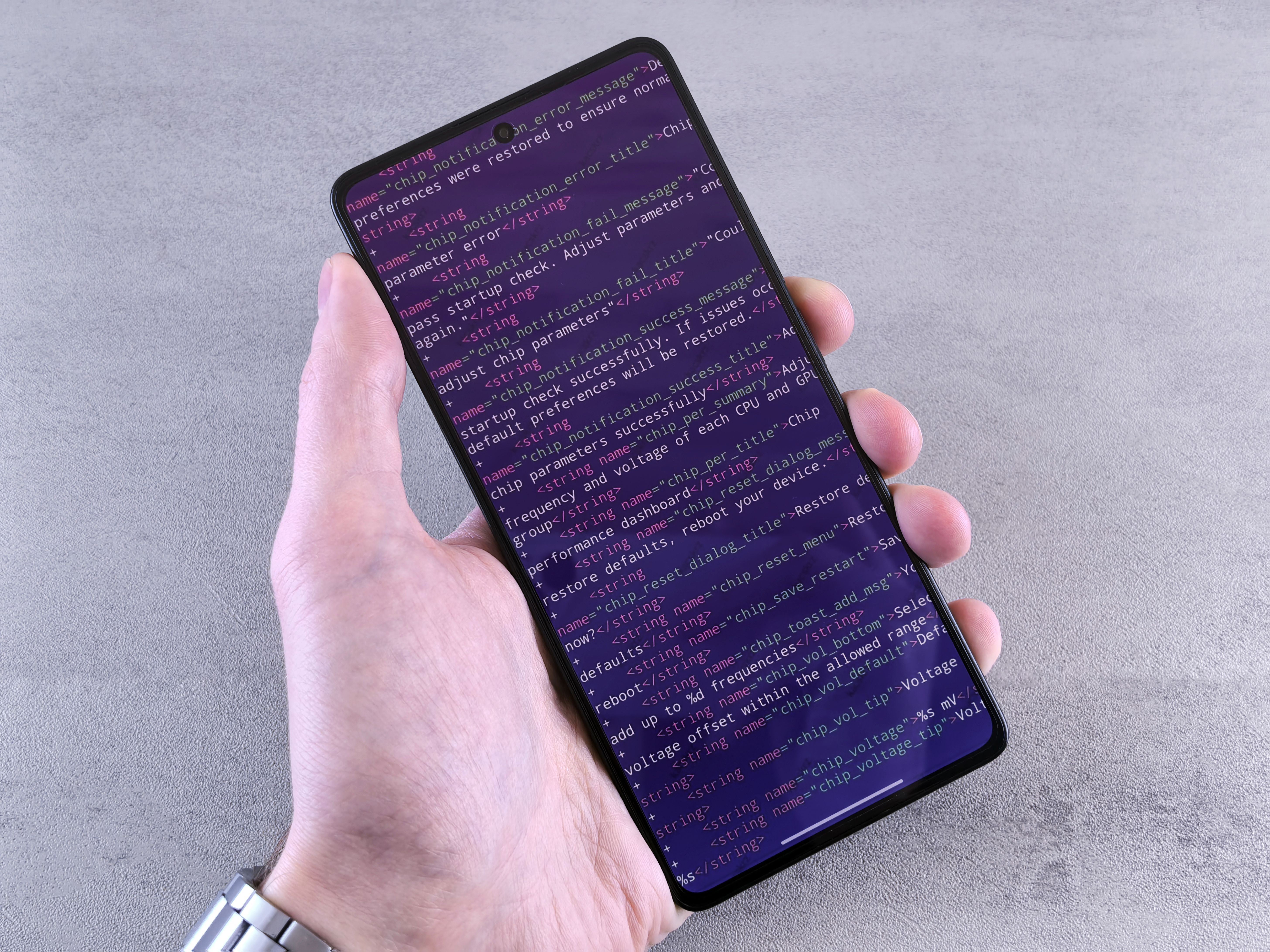 Close-up of a smartphone displaying code text held in a person's hand.