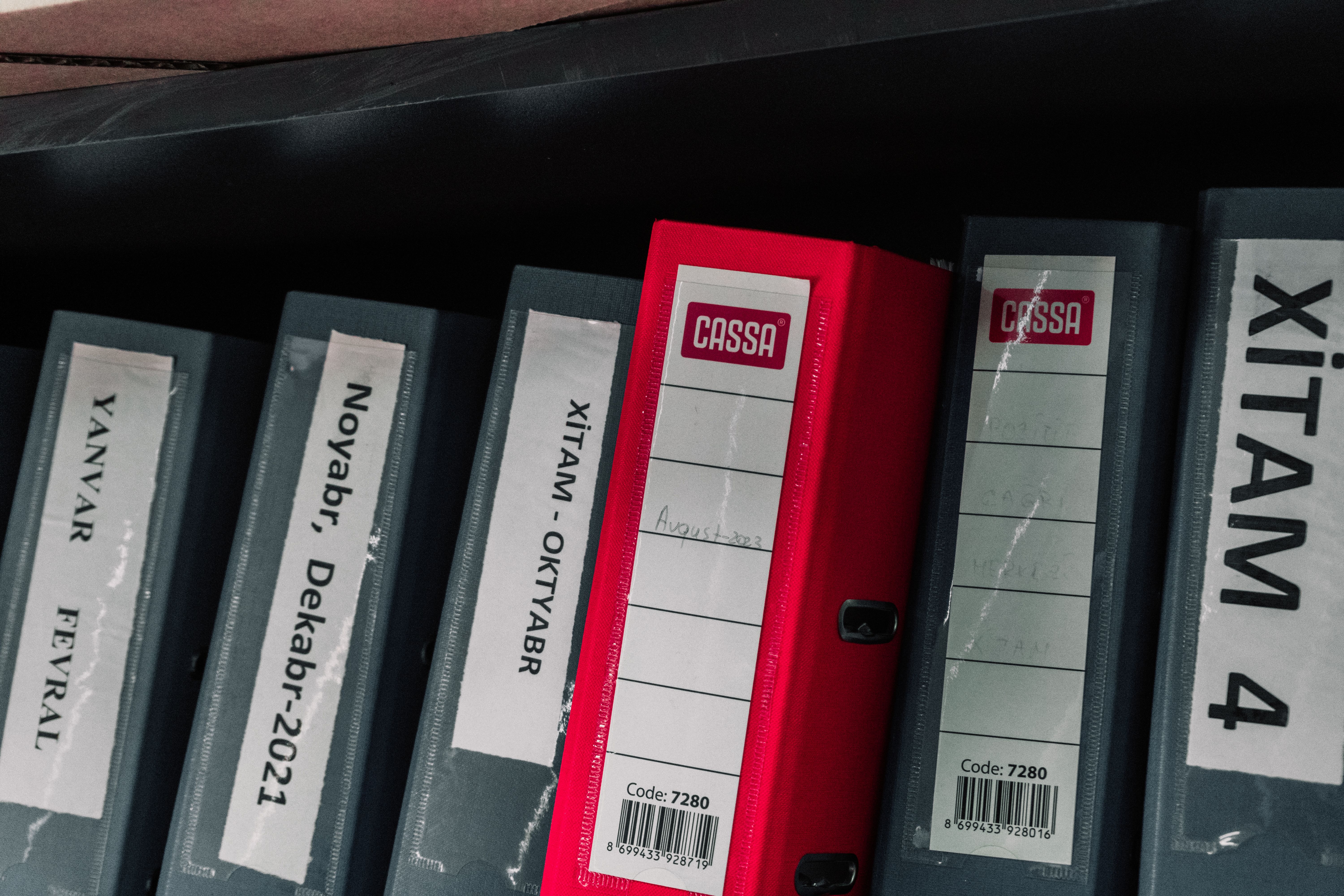 Color-coded office binders organized neatly in a storage shelf, featuring labels and a striking red binder.