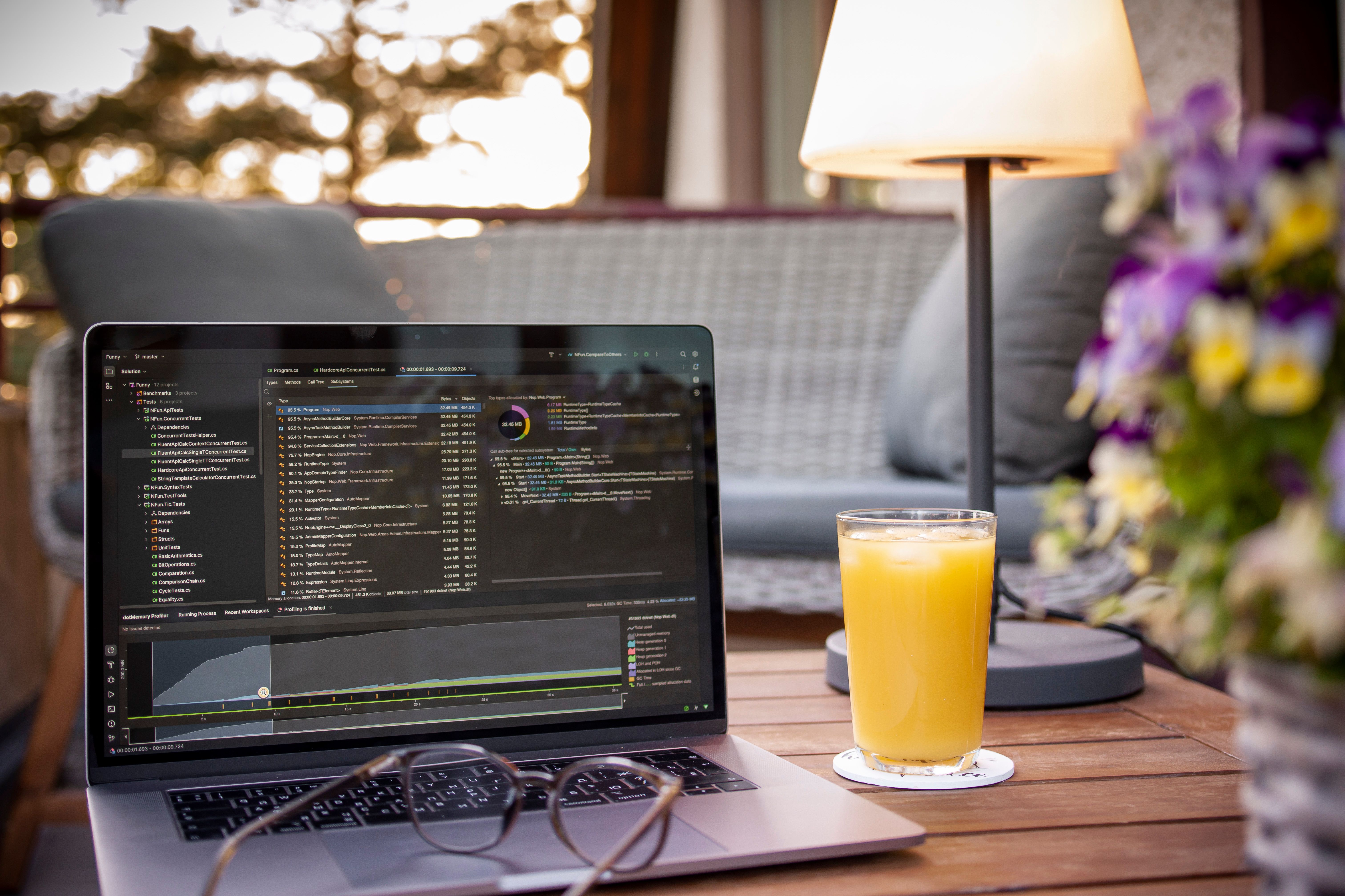 Laptop displaying code on a balcony with orange juice and flowers, under ambient light, perfect for work-from-home settings.