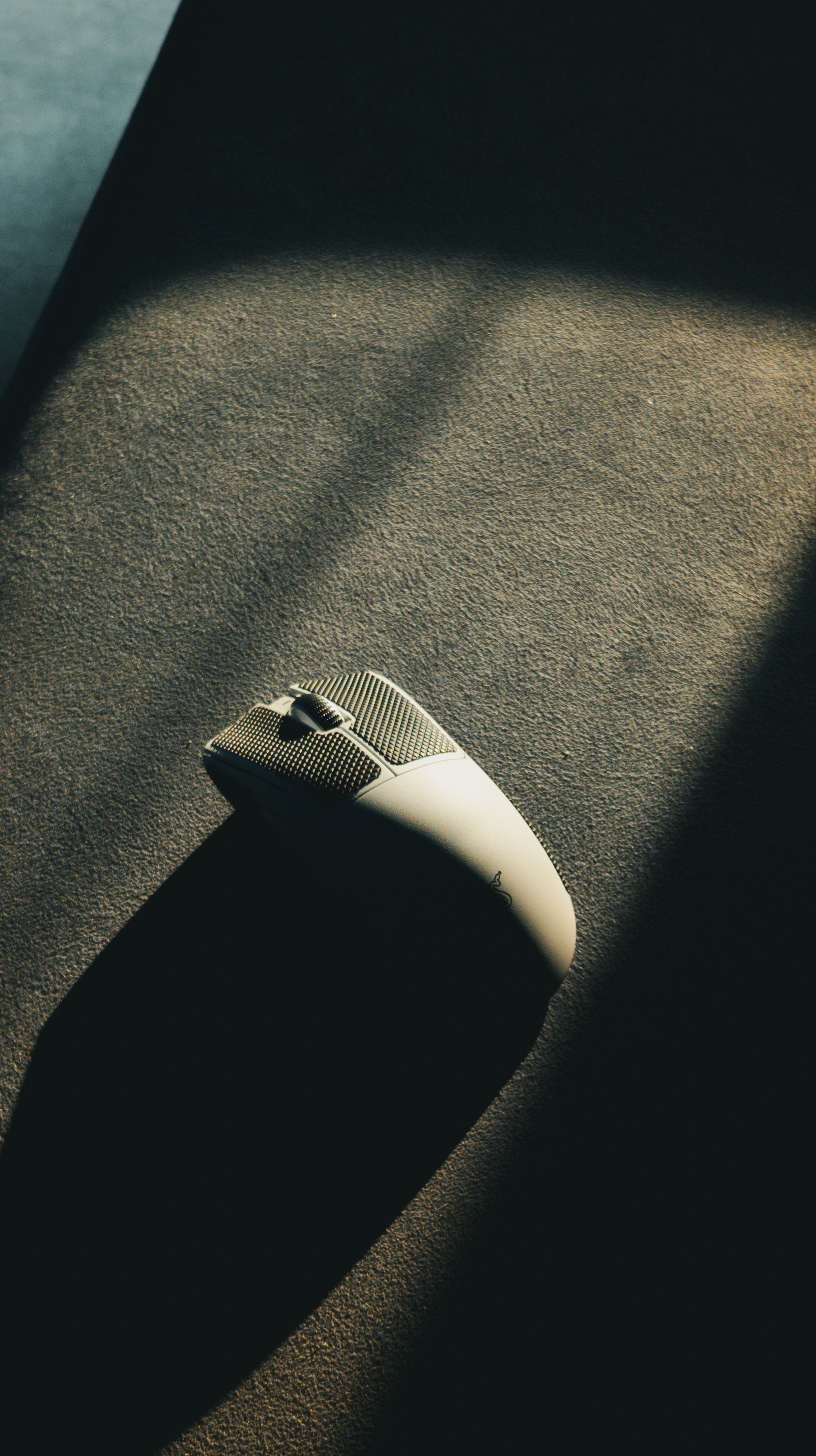 A sleek, illuminated computer mouse on a textured surface with dramatic lighting and shadows.