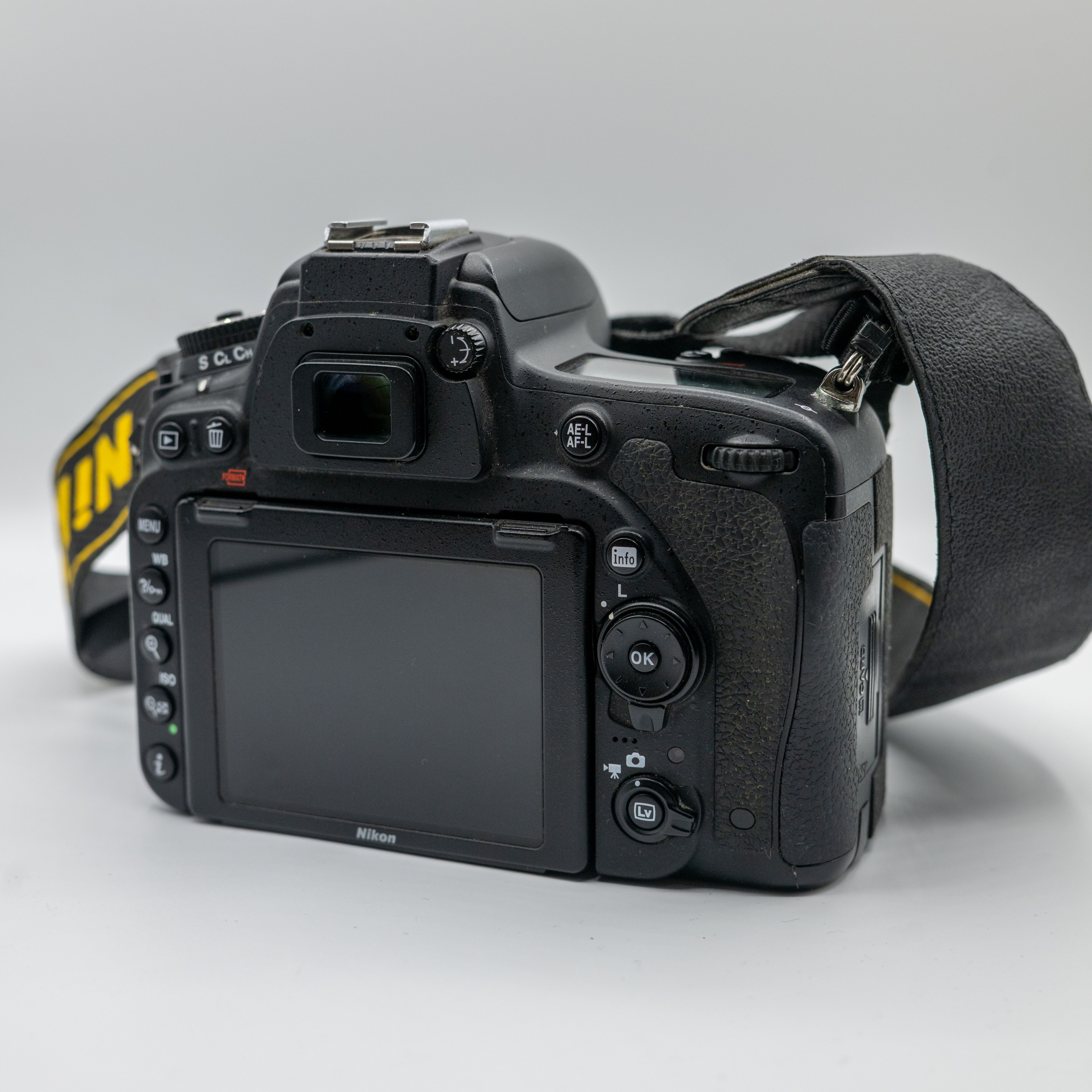 Close-up of a black DSLR camera with strap on a white surface, showing rear controls and screen.