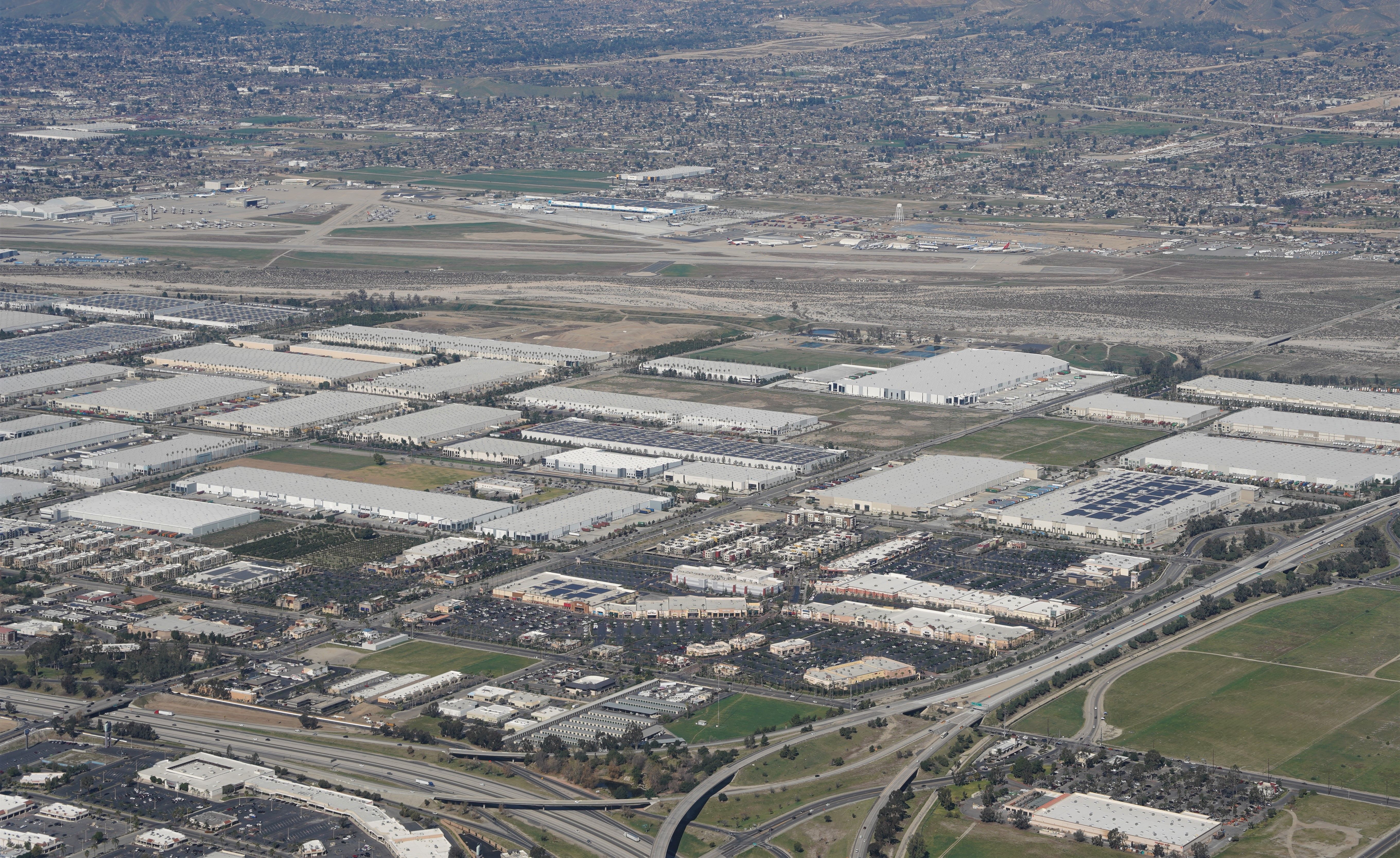 Expansive aerial shot of industrial area near a major airport and urban landscape.