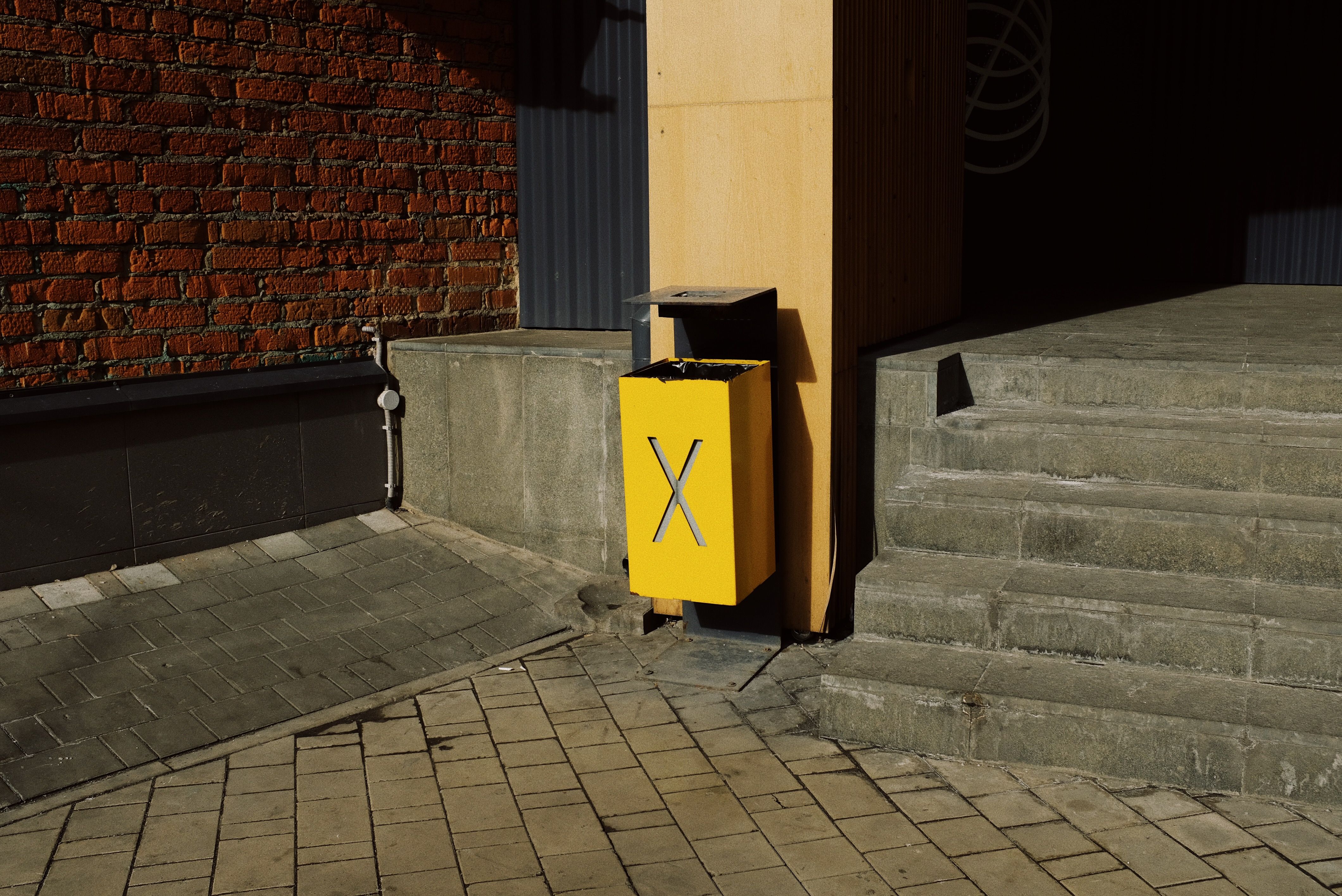 Yellow metal trash box placed near column and concrete stairs of modern building on street in city