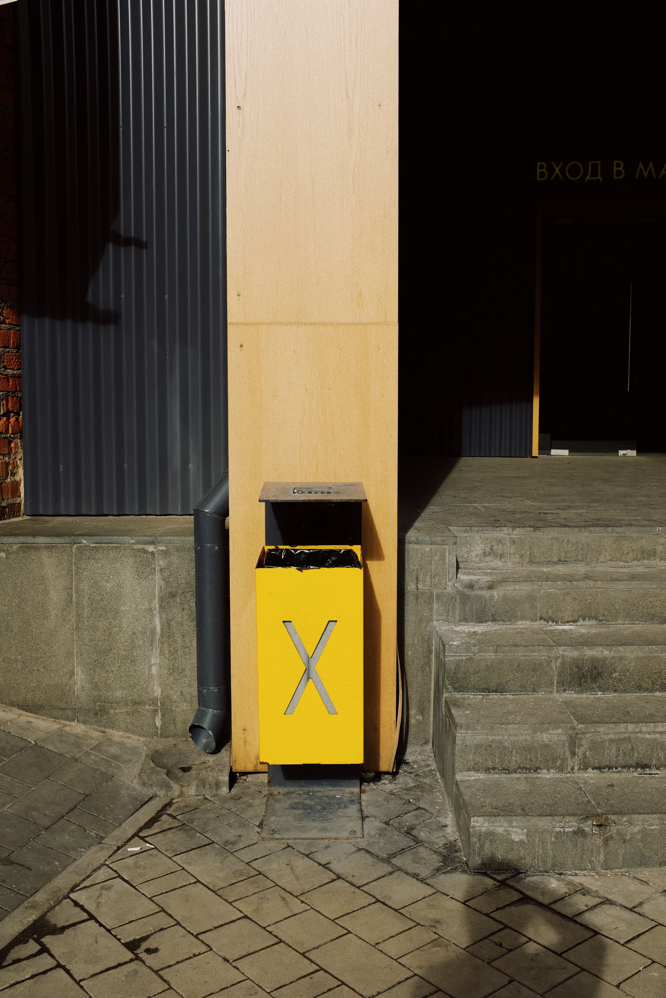 Street scene featuring a yellow trash bin next to concrete stairs at an entrance.