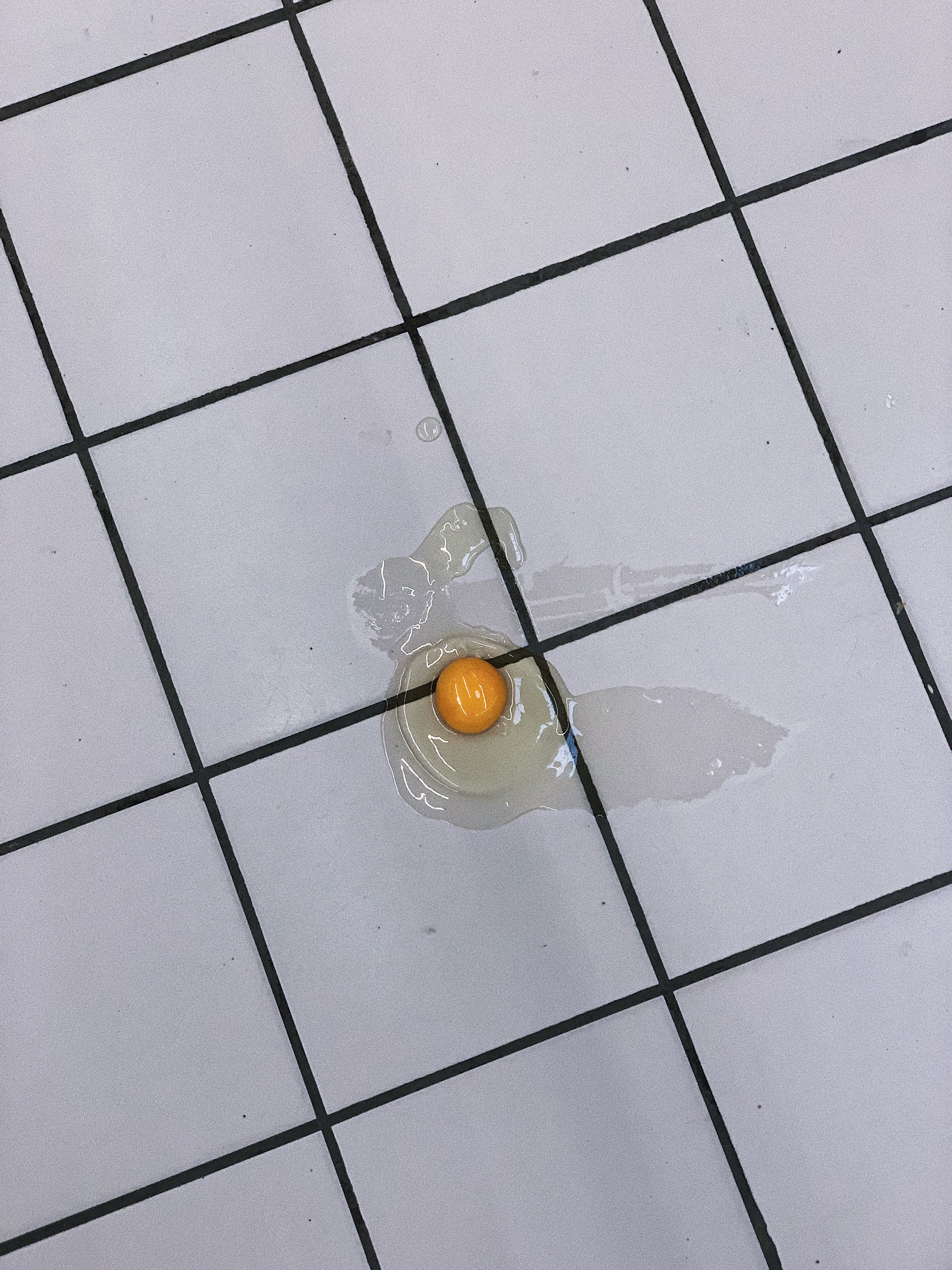 From above cracked uncooked egg without eggshell dropped on piled floor in kitchen
