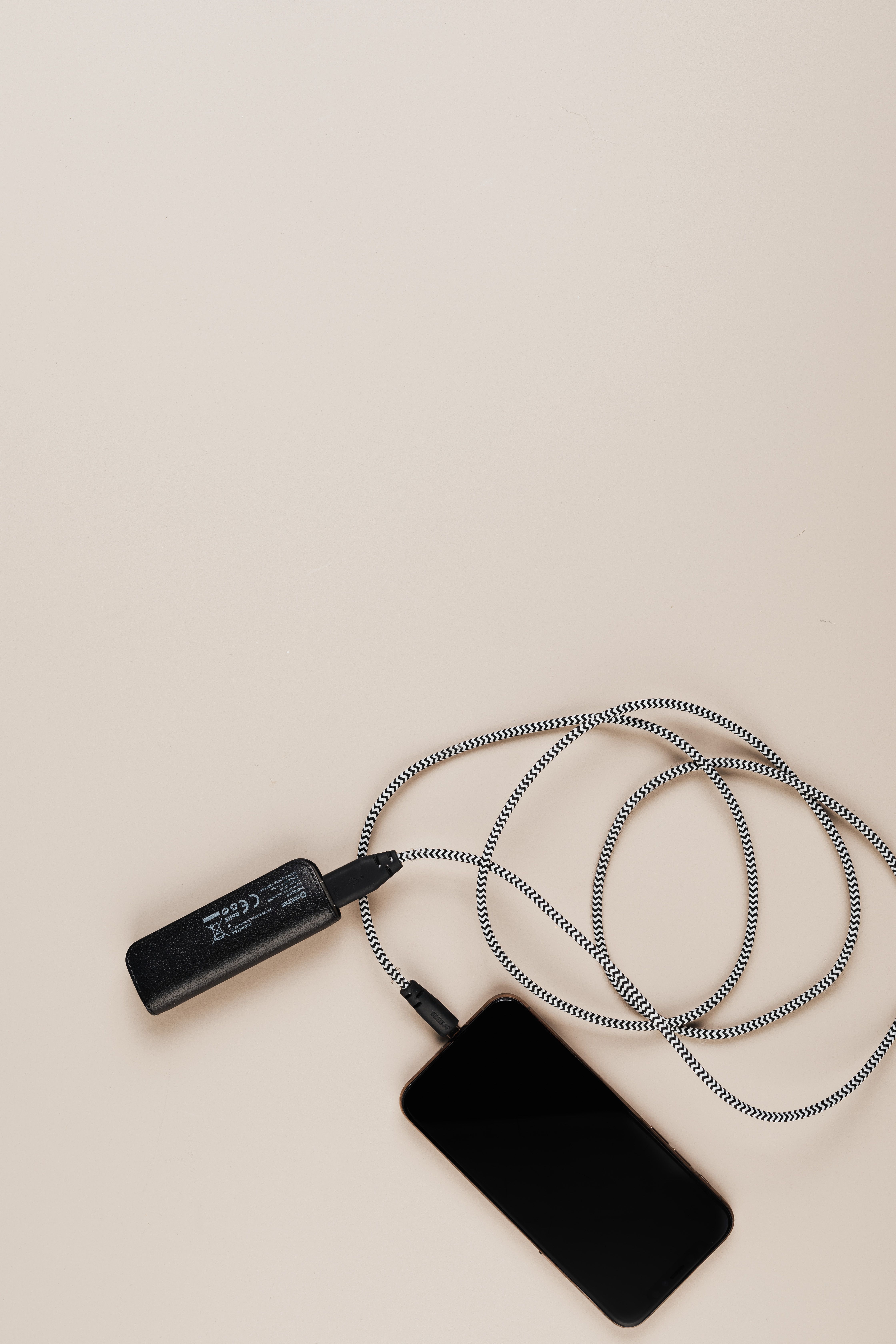 Overhead shot of a smartphone charging with a power bank on a plain background.