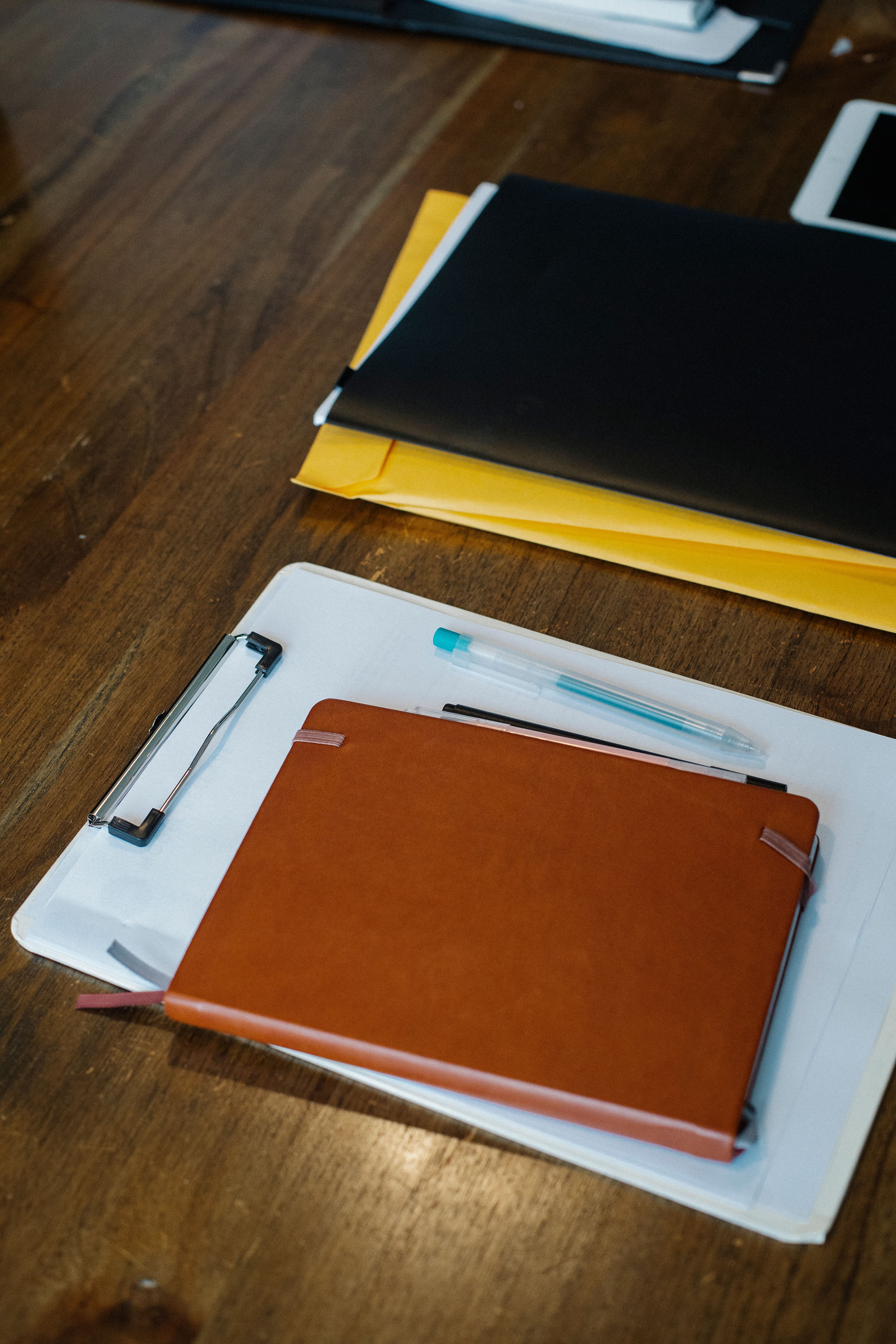 From above of leather planner placed on clipboard with blank paper sheets arranged on wooden table with document folders in office