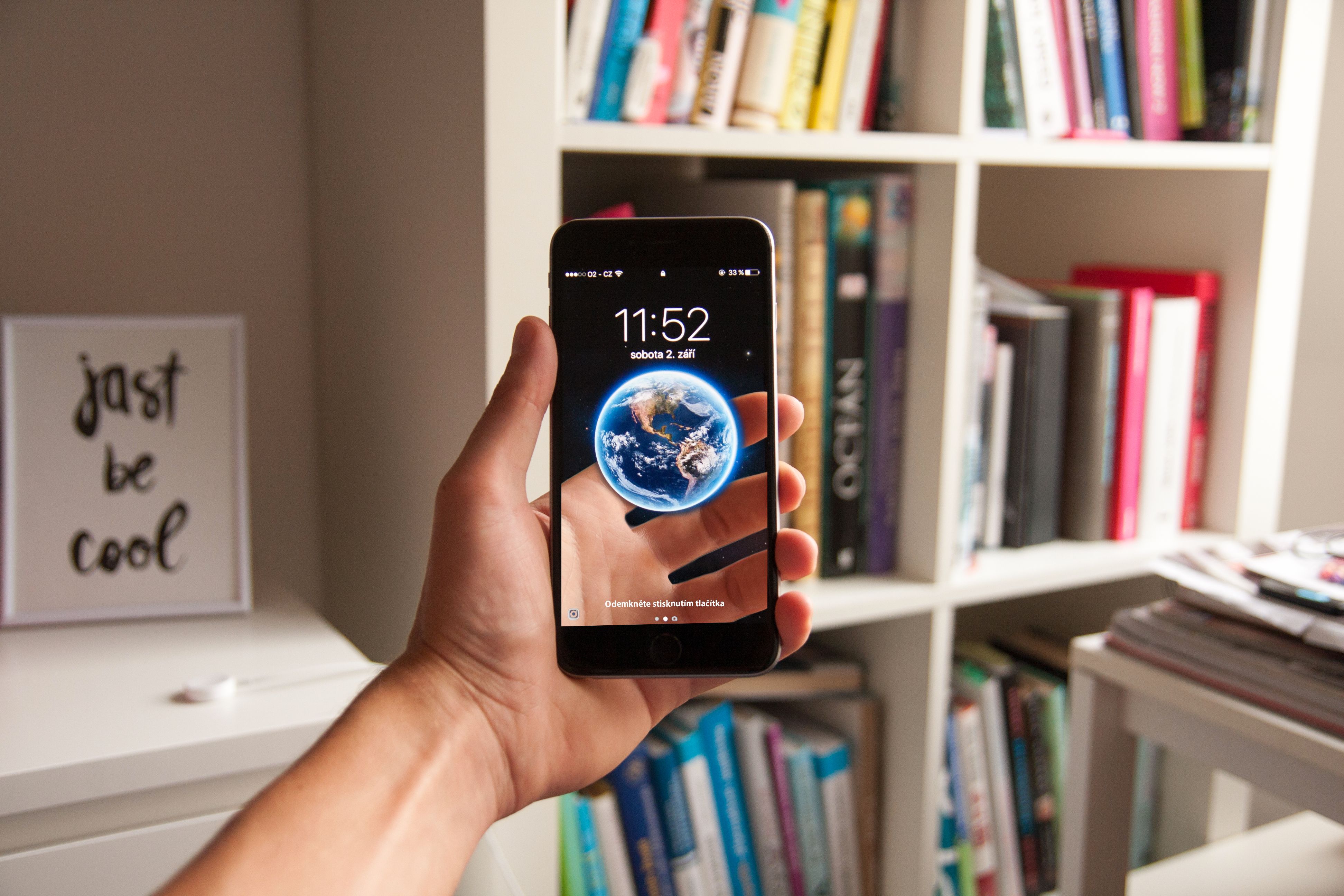 Hand holding smartphone with earth wallpaper, surrounded by books in a study room.