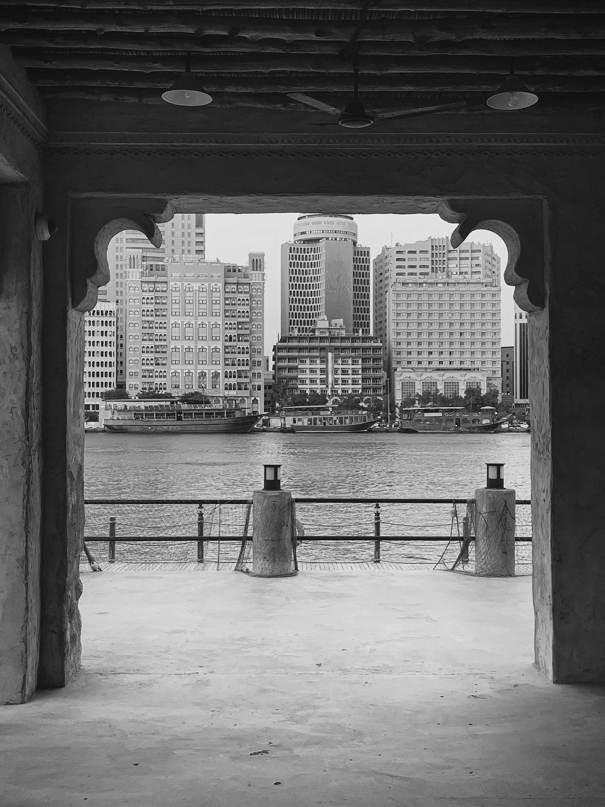 Grayscale view of modern city buildings framed by traditional archway over water.