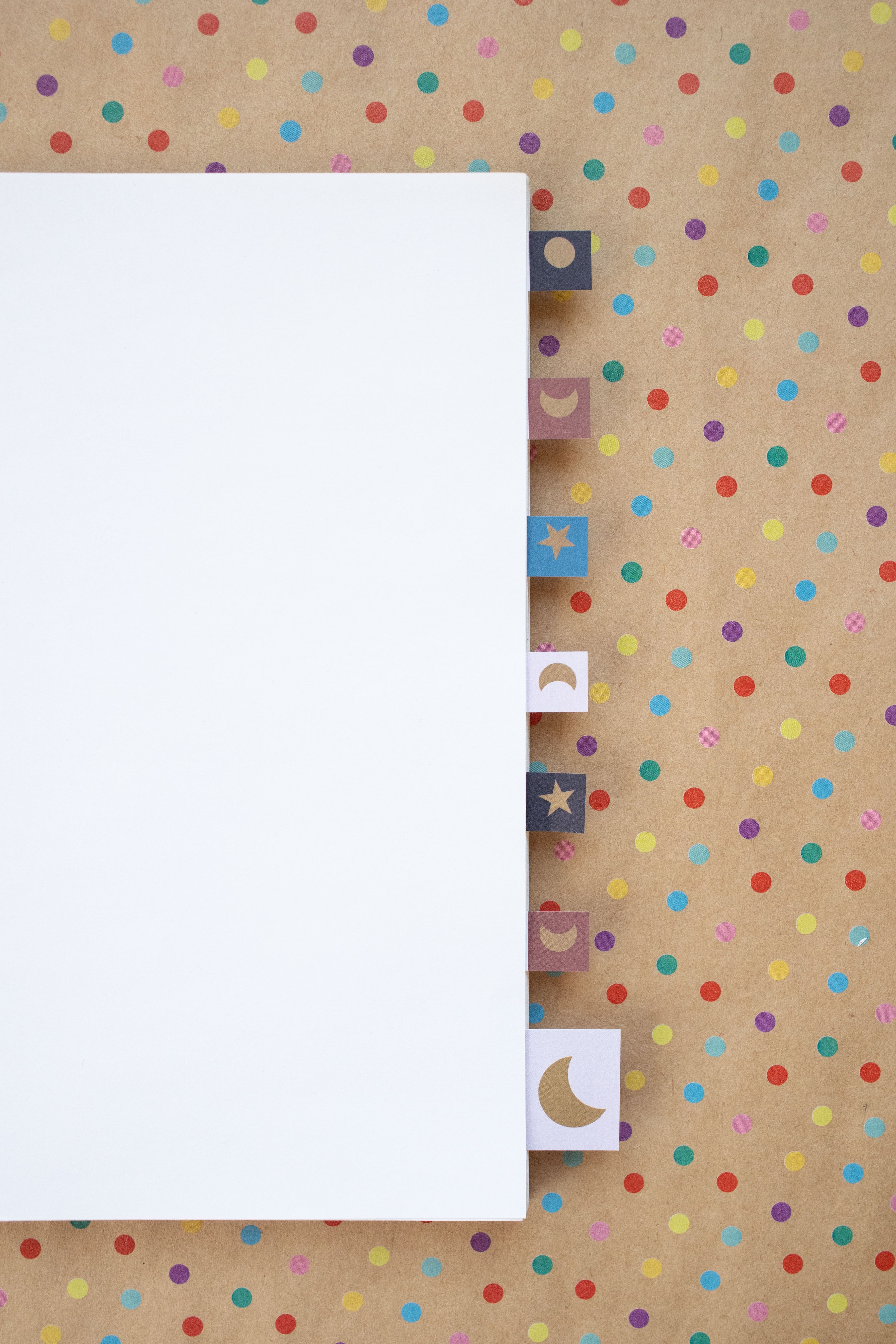Notebook with colorful tabs on a vibrant polka dot paper background, ideal for stationery and design concepts.
