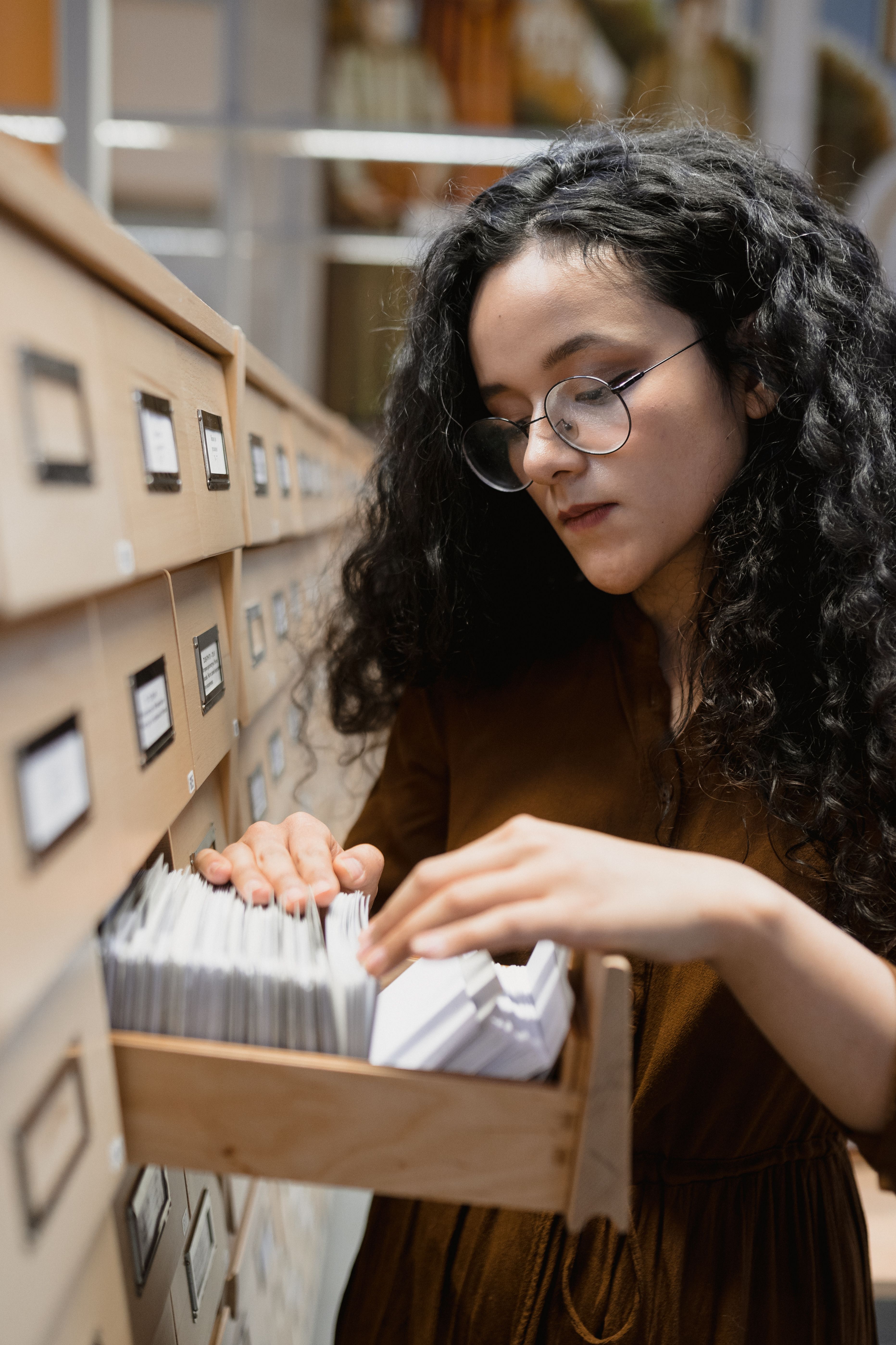 Young woman with glasses searching in a card catalog in a library.