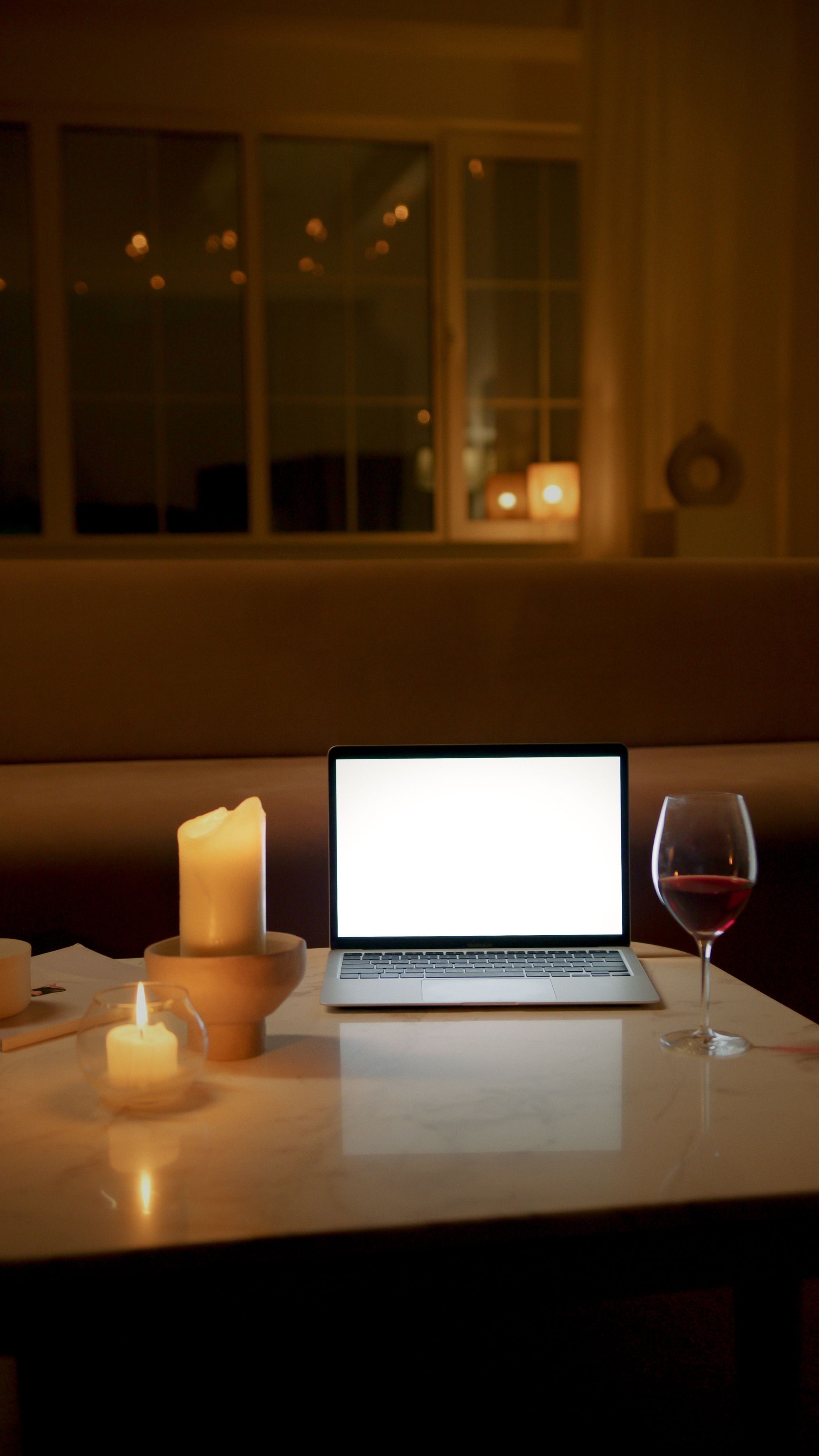 A cozy evening setting featuring a laptop, candles, and a glass of wine on a table.