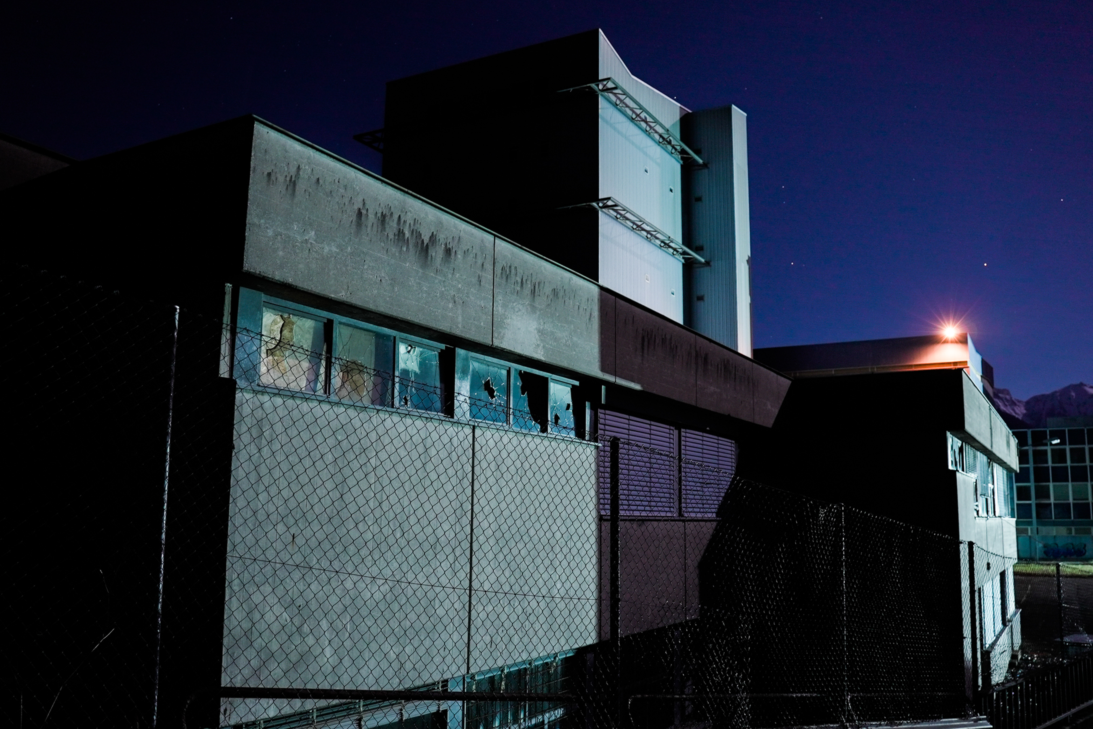 A dark view of an abandoned factory at night, showcasing broken windows and eerie atmosphere.