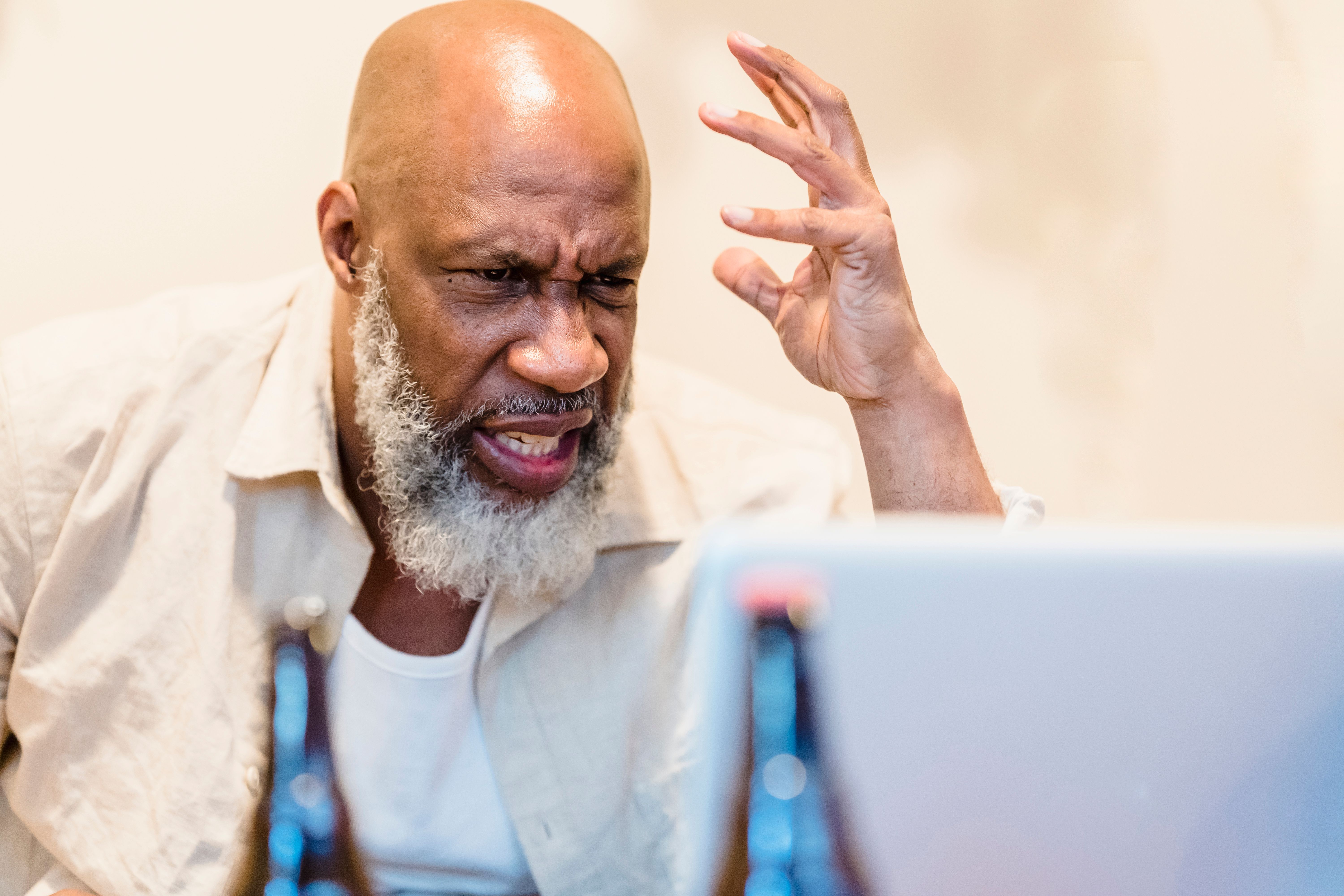 An adult man expressing frustration during a video call with a laptop indoors.