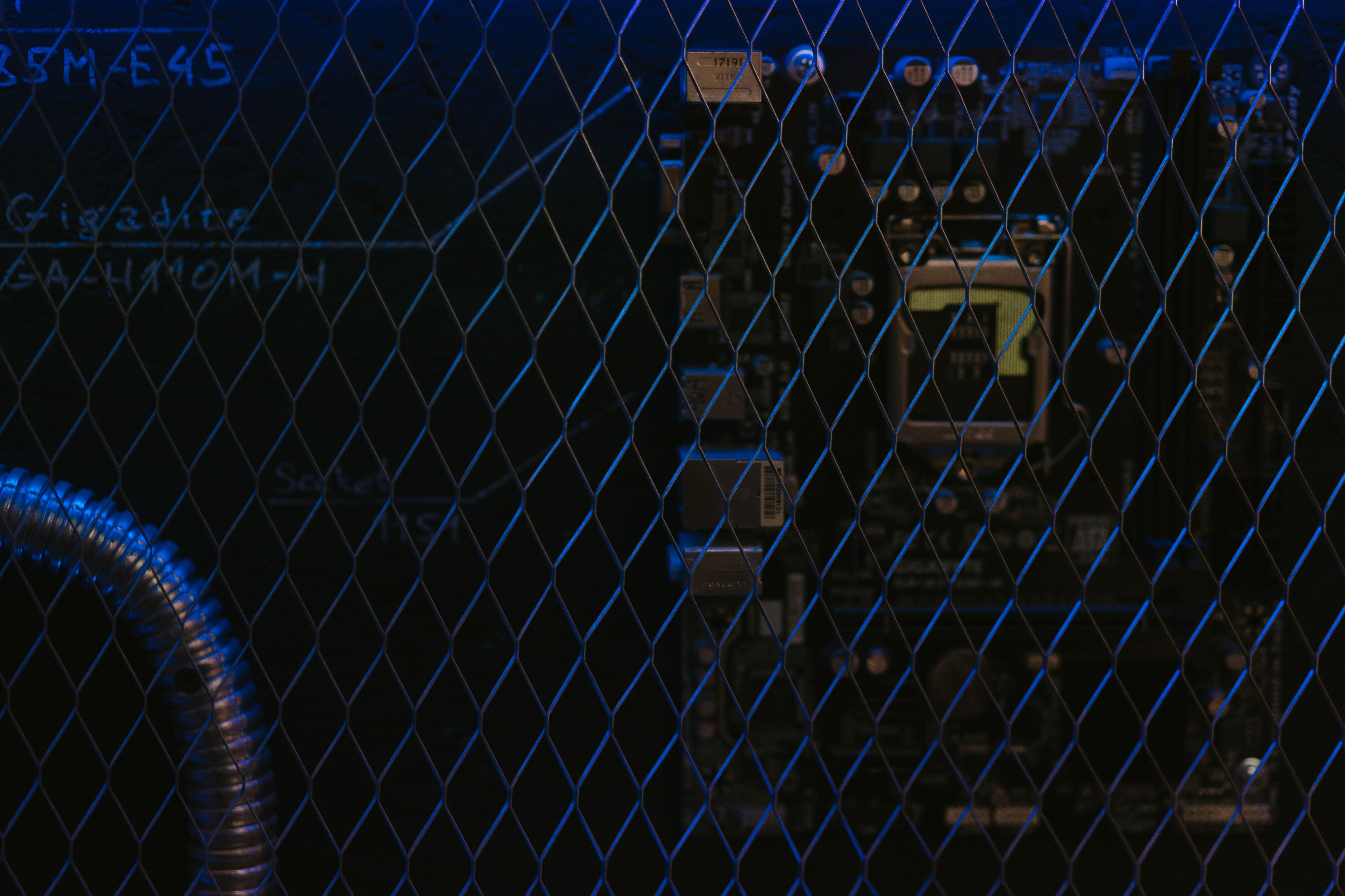 Artistic view of a circuit board through metal mesh with blue lighting.