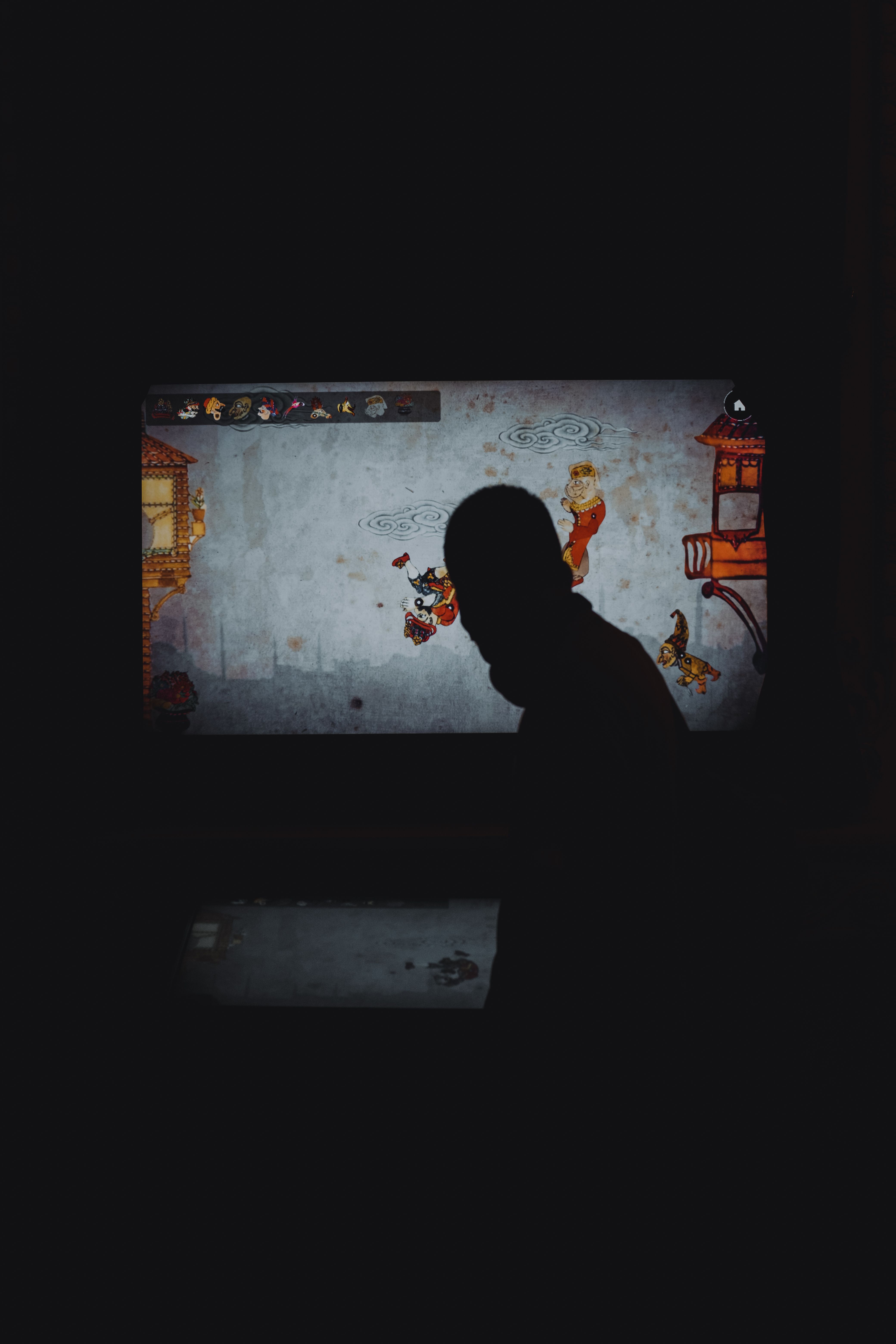 A person's silhouette in front of a colorful video game display in low light.